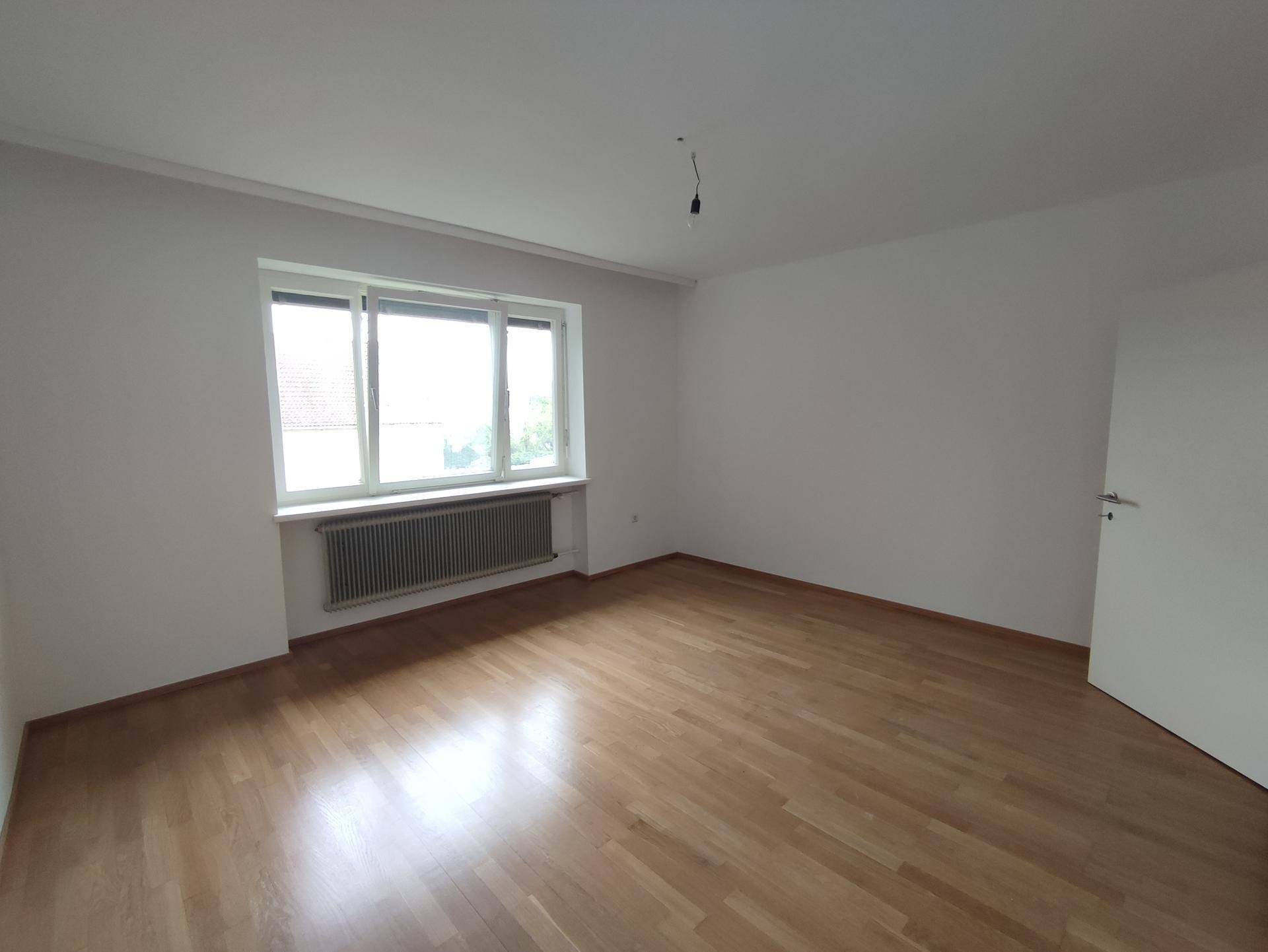 Helles Schlafzimmer mit Holzdielenboden, großem Fenster und Blick ins Grüne.
