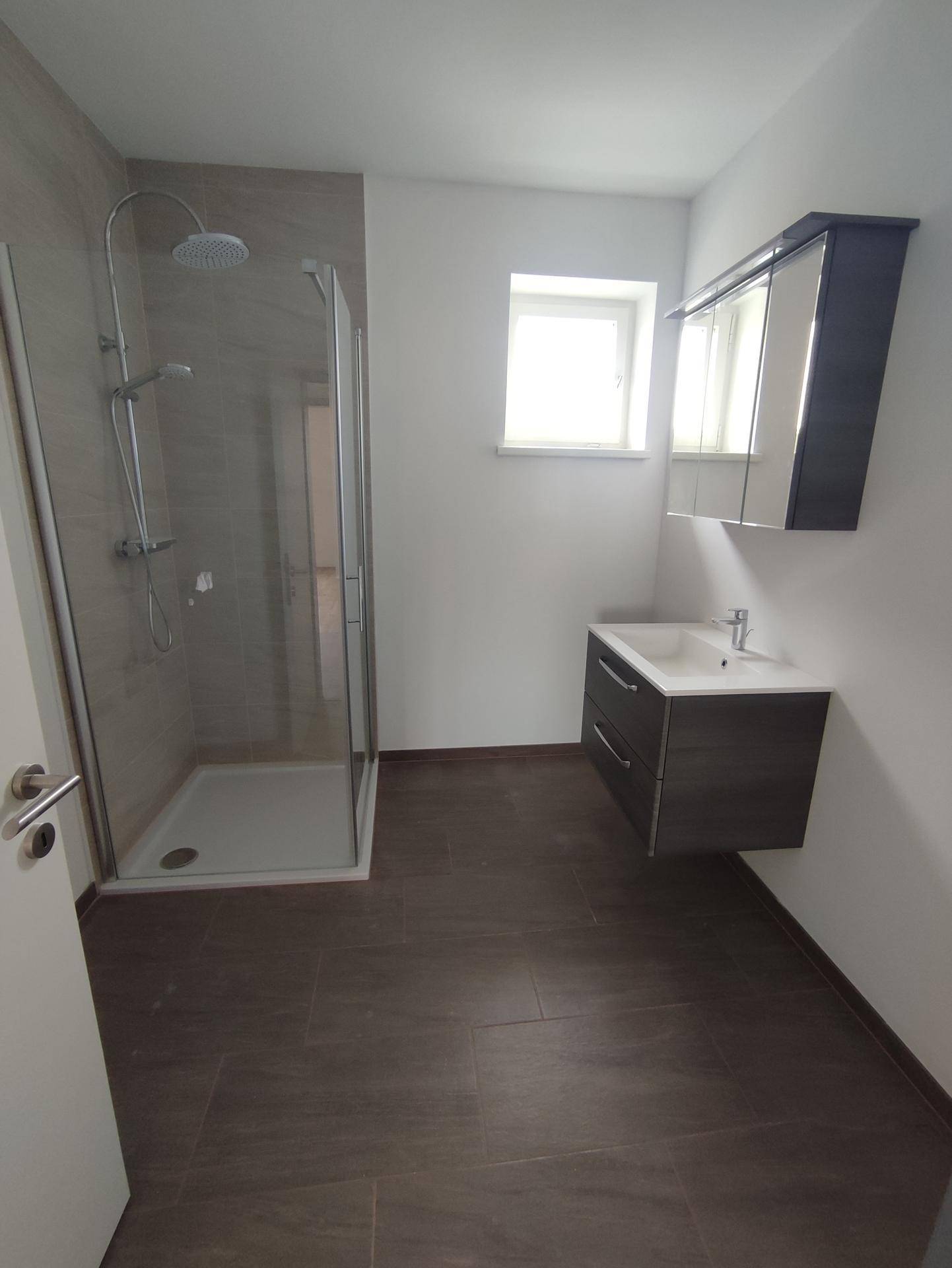 Modernes Badezimmer mit Dusche, Waschtisch, Spiegelschrank und Fenster für Tageslicht.