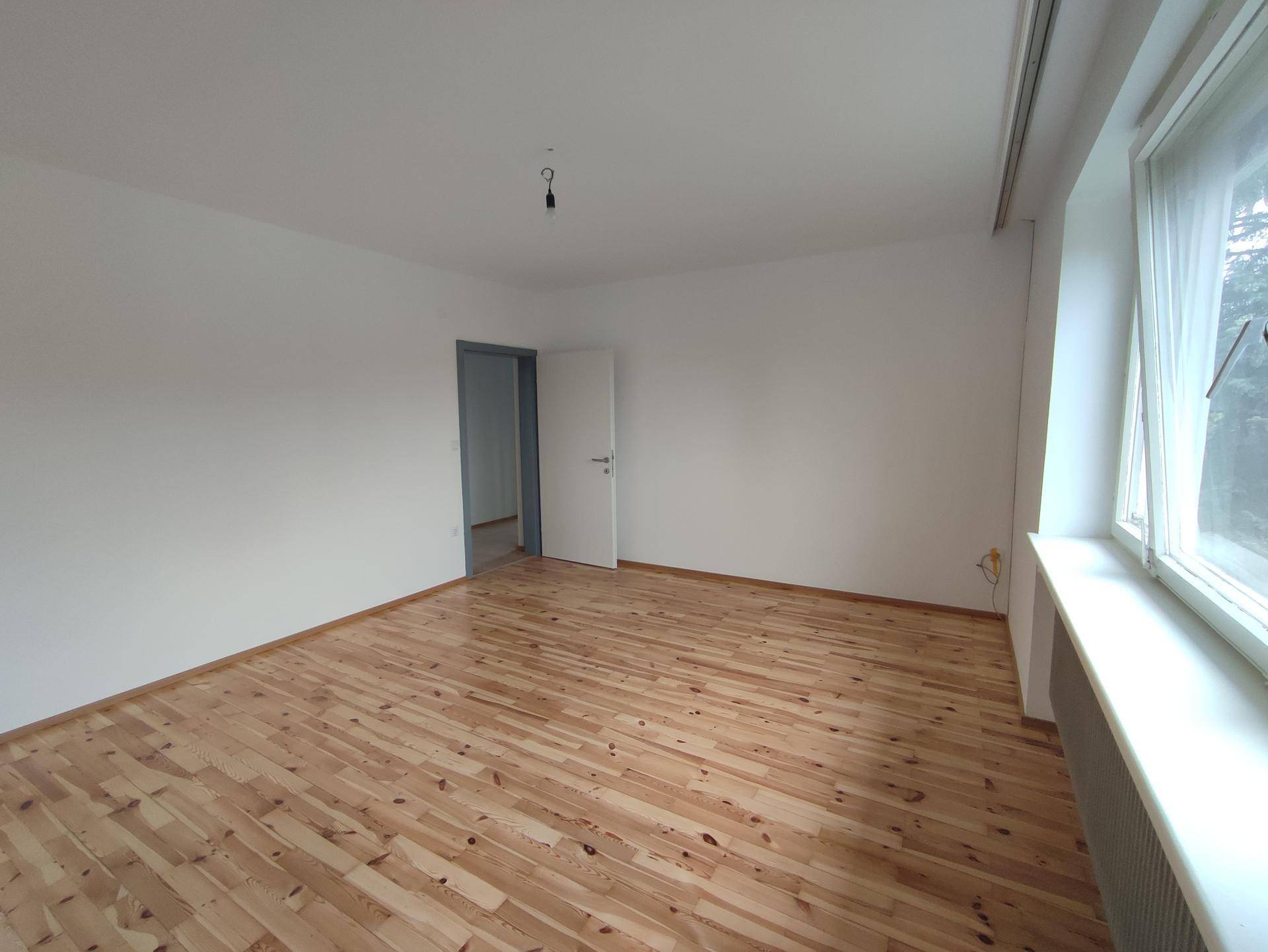 Geräumiges Zimmer mit hellem Holzdielenboden, großen Fenstern und viel Tageslicht.