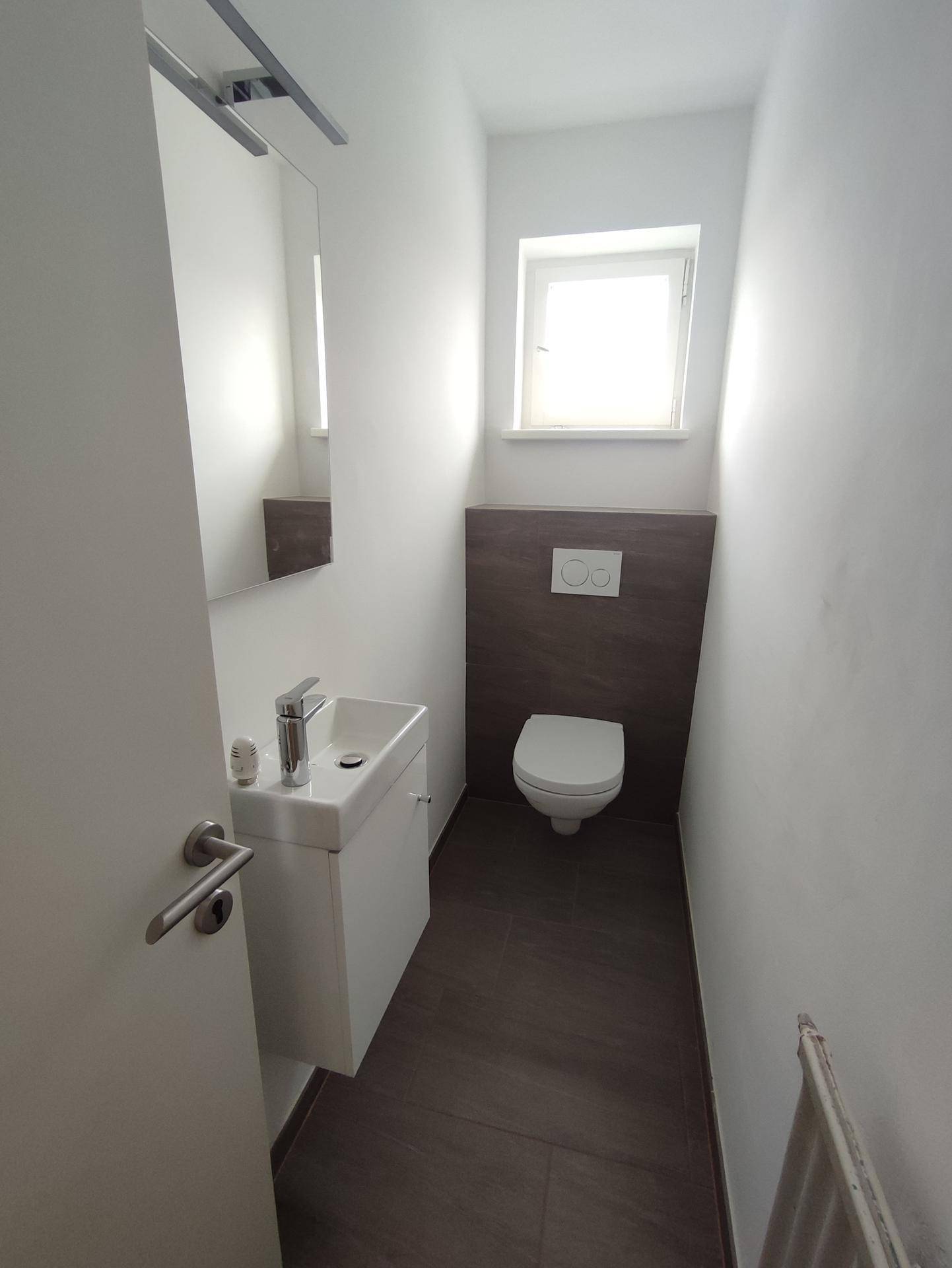 Kleines Gäste-WC mit wandhängendem WC, Waschtisch und Fenster für Belüftung.