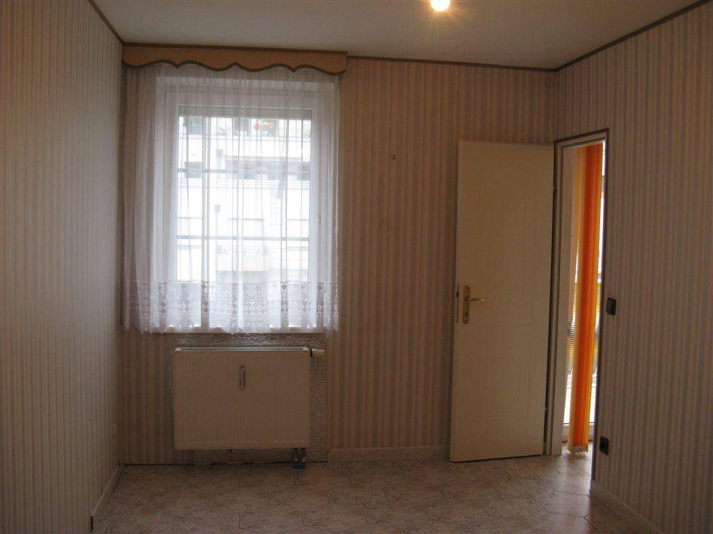 Leeres Schlafzimmer mit gestreifter Tapete, Fenster und Heizkörper, bereit zur individuellen Gestaltung.