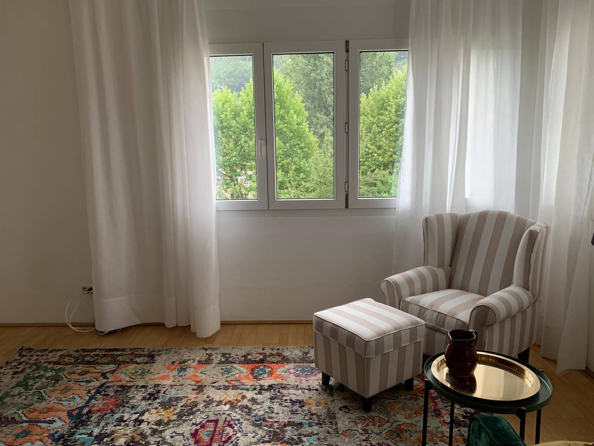 Gemütlicher Sessel am Fenster mit Blick ins Grüne und hellen Vorhängen.
