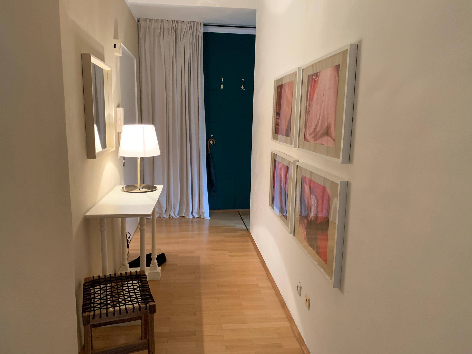 Heller Flur mit Konsole, Spiegel, Kunstwerken und dunkler Akzenttür.