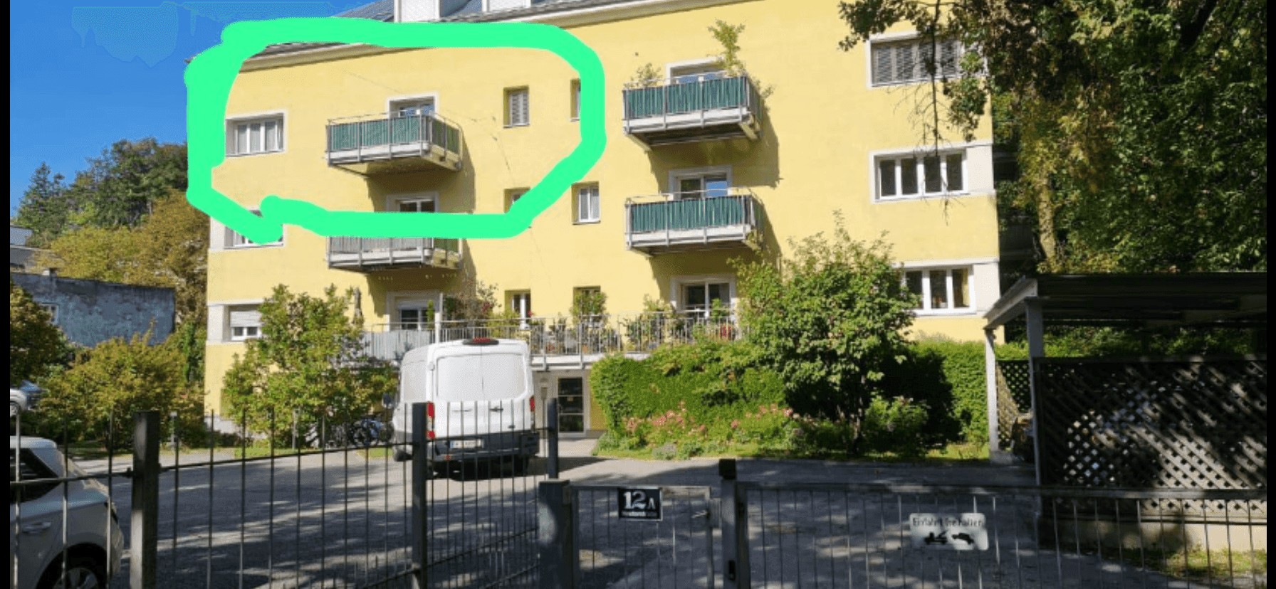 Gelbes Mehrfamilienhaus mit mehreren Balkonen und grüner Umgebung.