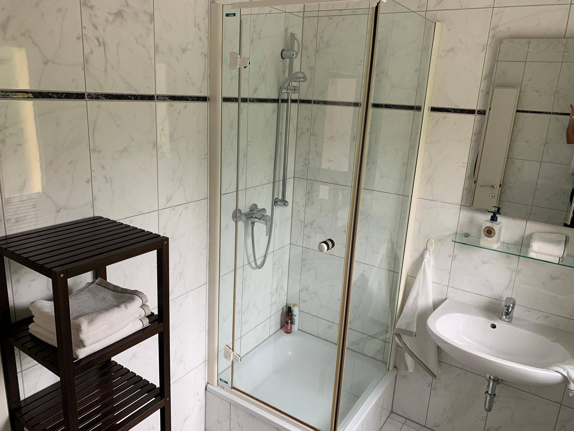 Modernes Badezimmer mit Duschkabine, Waschbecken und hellen Marmorfliesen.