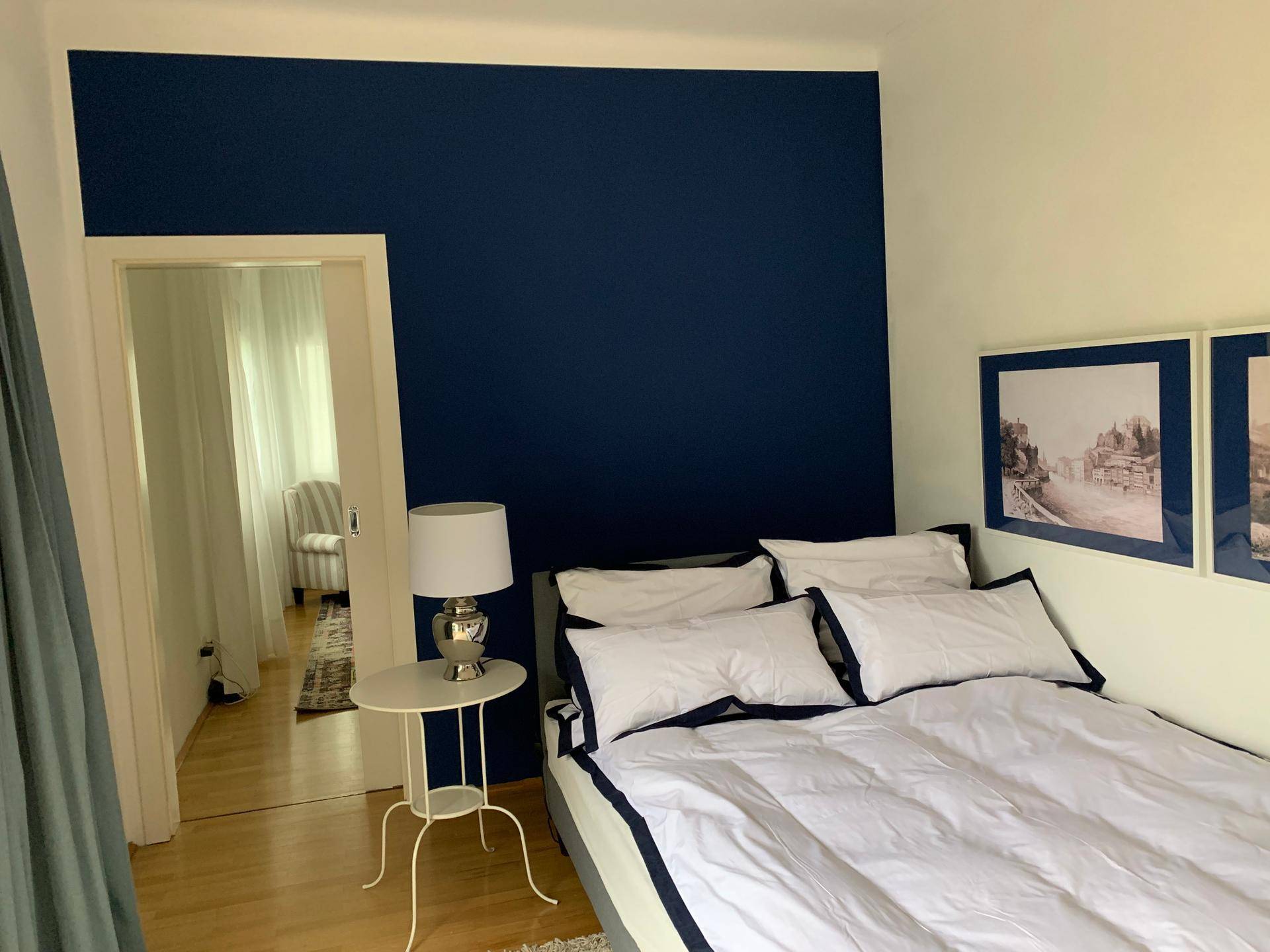 Schlafzimmer mit blauer Wand und Zugang zu einem weiteren hellen Wohnbereich.