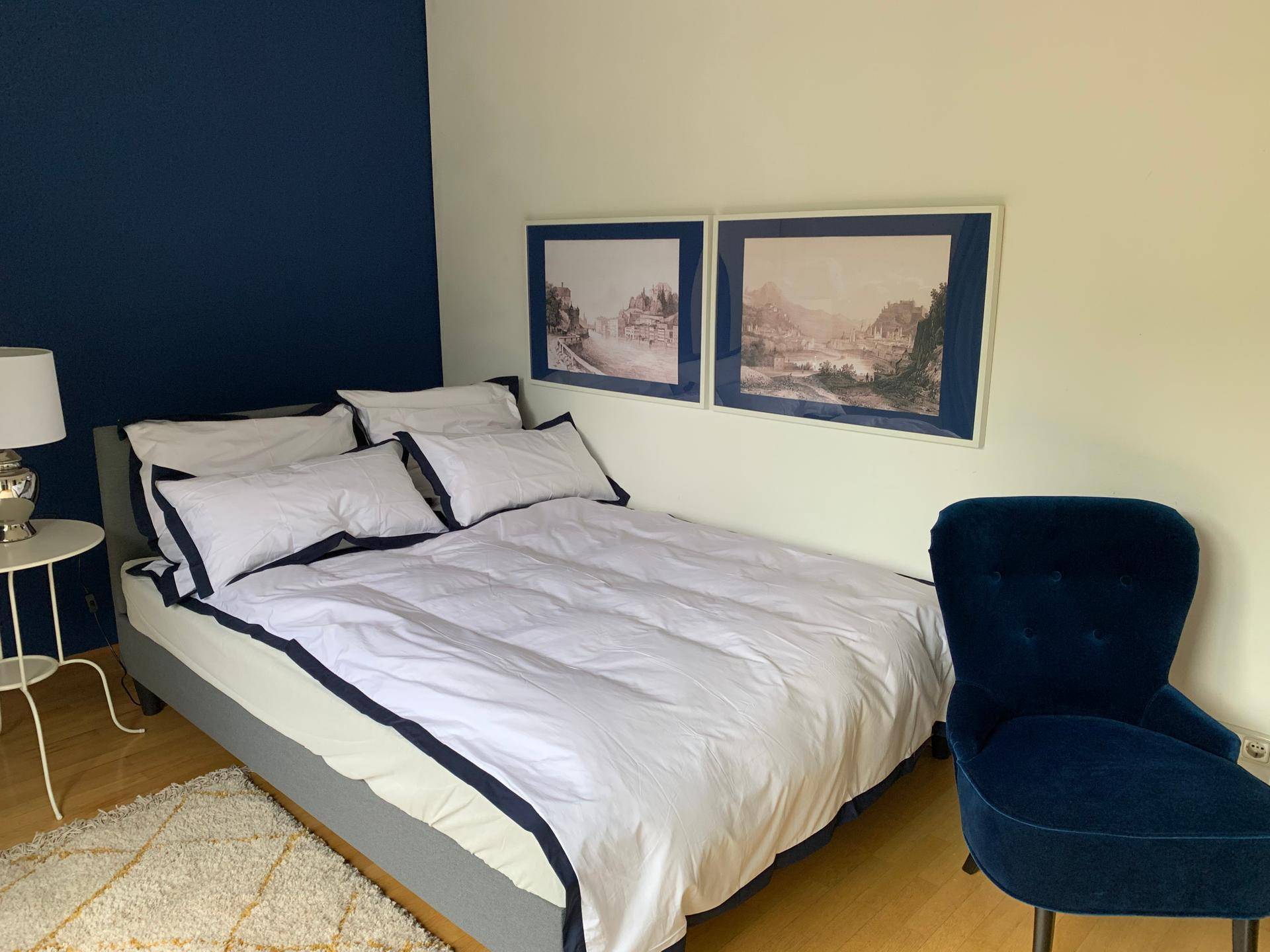 Schlafzimmer mit blauer Akzentwand, Doppelbett und stilvollem blauen Samtsessel.