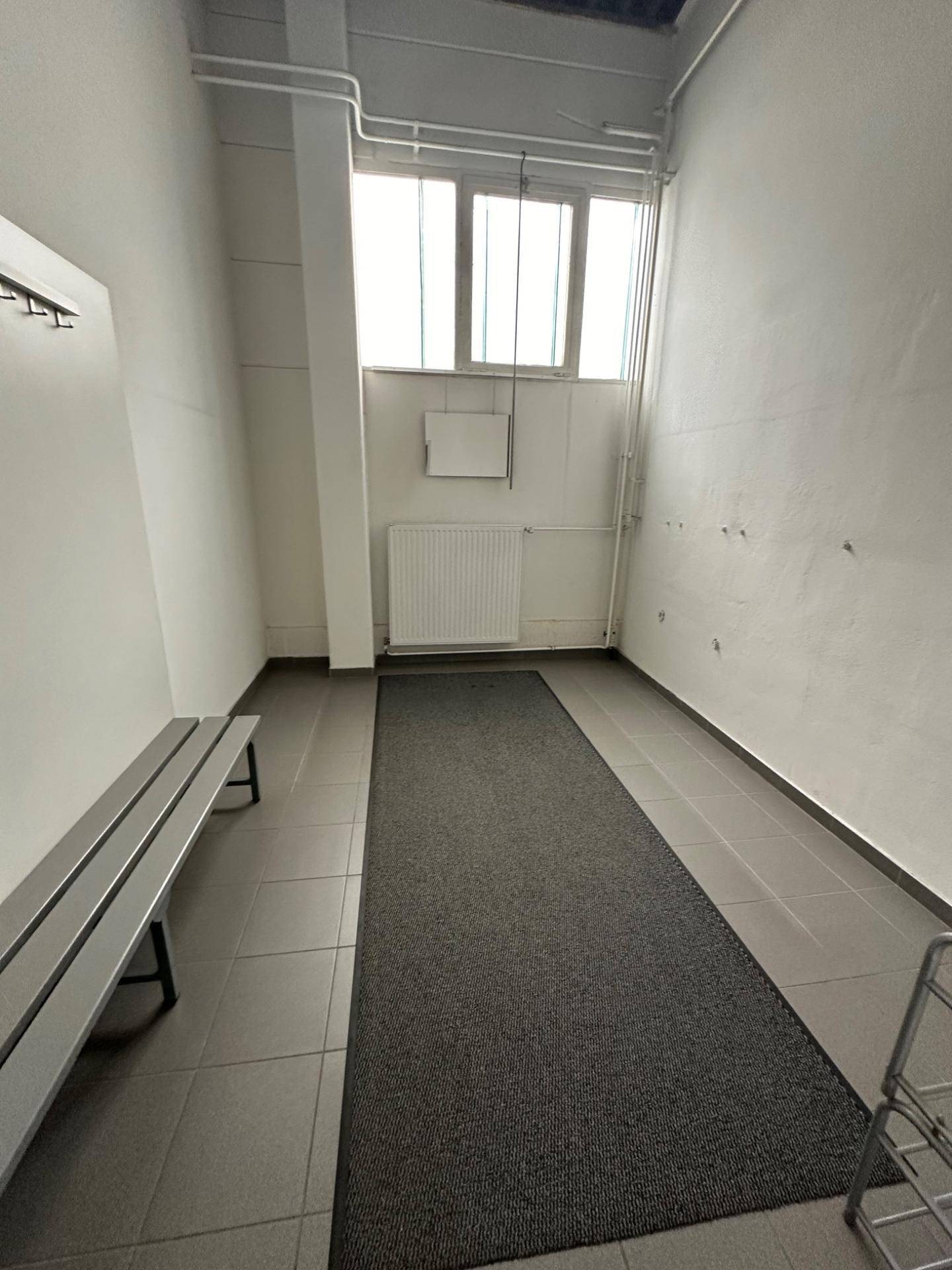 Umkleideraum mit Fliesenboden, einer Bank und einem Heizkörper unter einem Fenster für Belüftung.