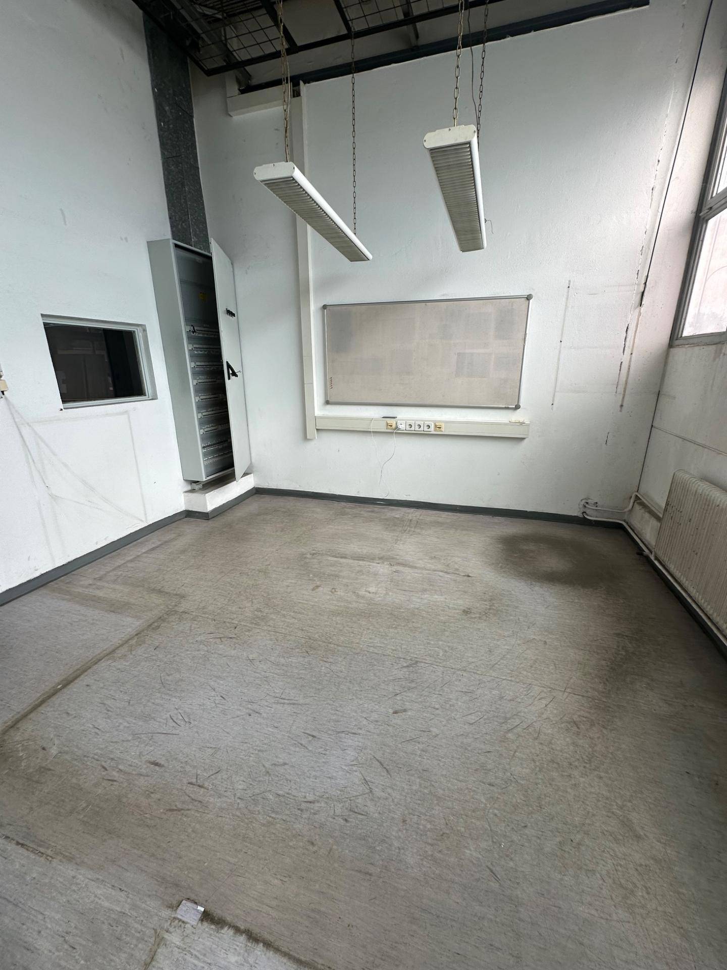 Einfacher Büroraum mit Betonboden, hohen Decken und einer Tafel an der Wand für Notizen.