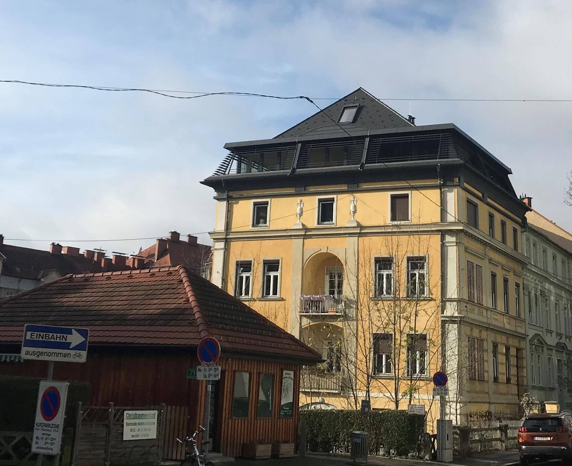 Gelbes Mehrfamilienhaus mit Balkonen, markantem Dach und umliegender Stadtansicht.