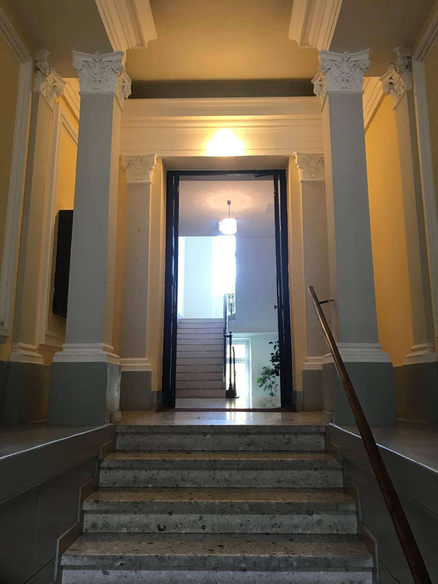 Repräsentativer Eingangsbereich mit breiter Treppe, klassischen Säulen und hohen Decken.