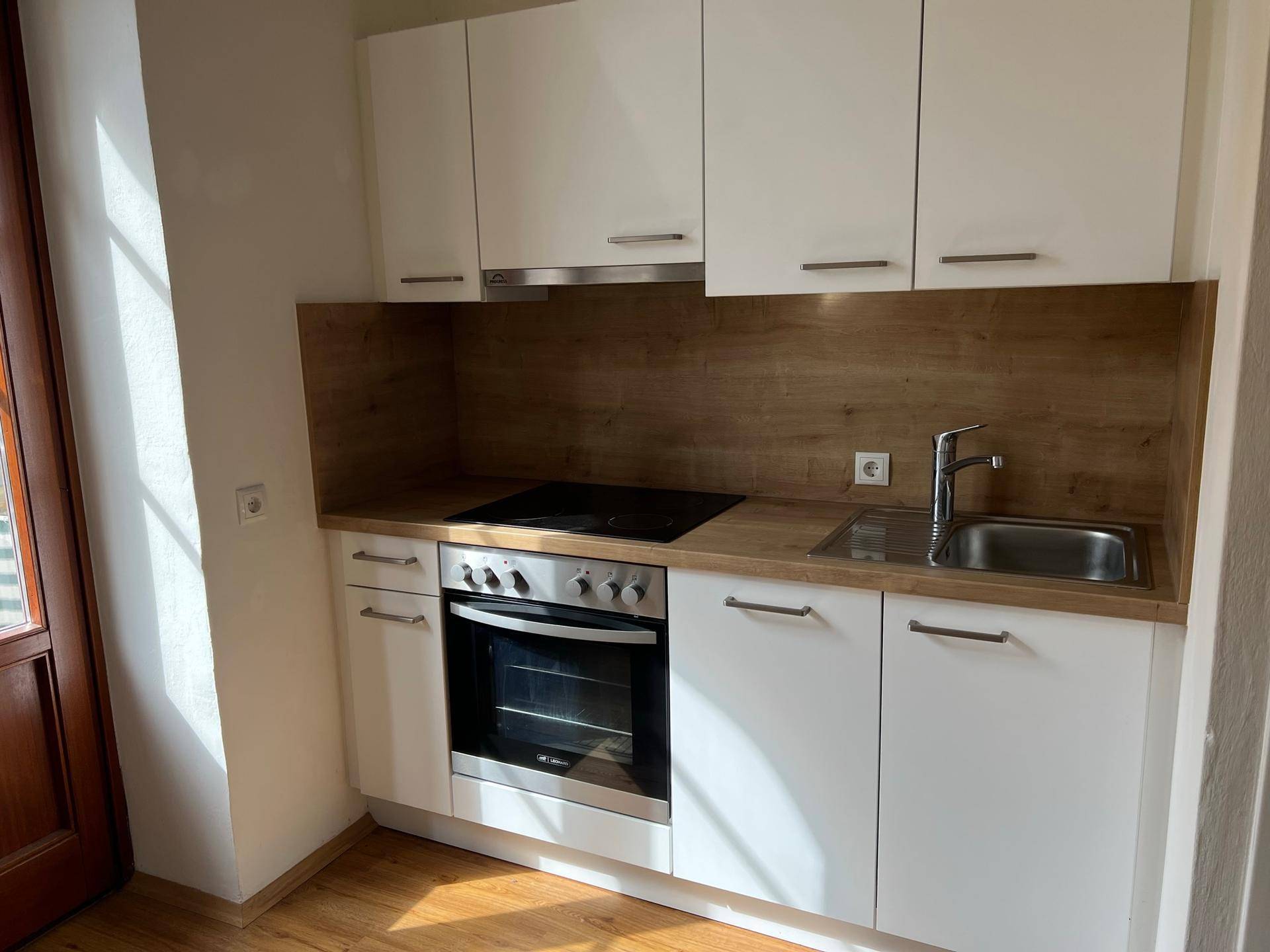 Moderne Einbauküche mit weißen Schränken, Holzoptik-Arbeitsplatte und integrierten Geräten.