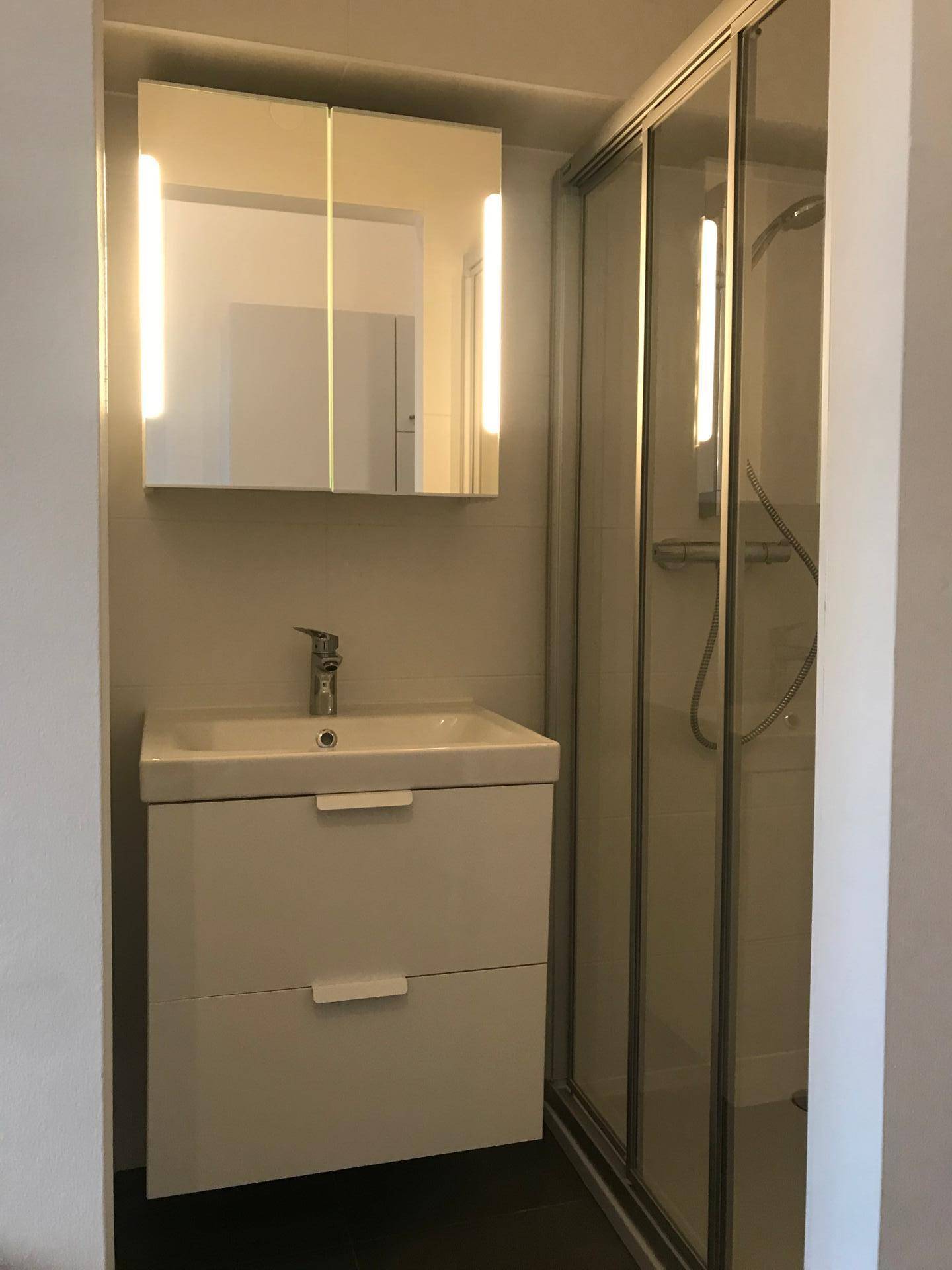 Kompaktes Badezimmer mit modernem Waschtisch, Spiegelschrank und Duschkabine.