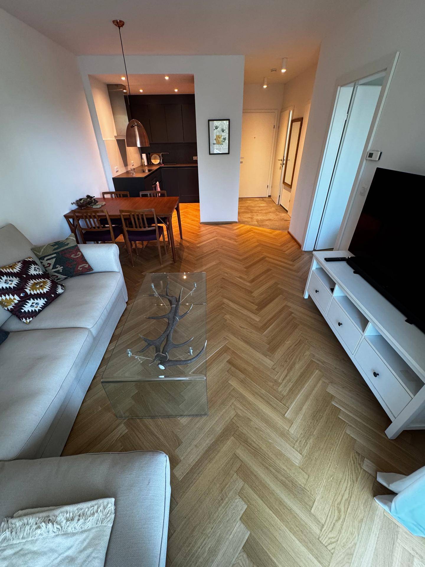 Offener Wohnbereich mit Fischgrätparkett, Sofa und Blick in die angrenzende, moderne Küche.