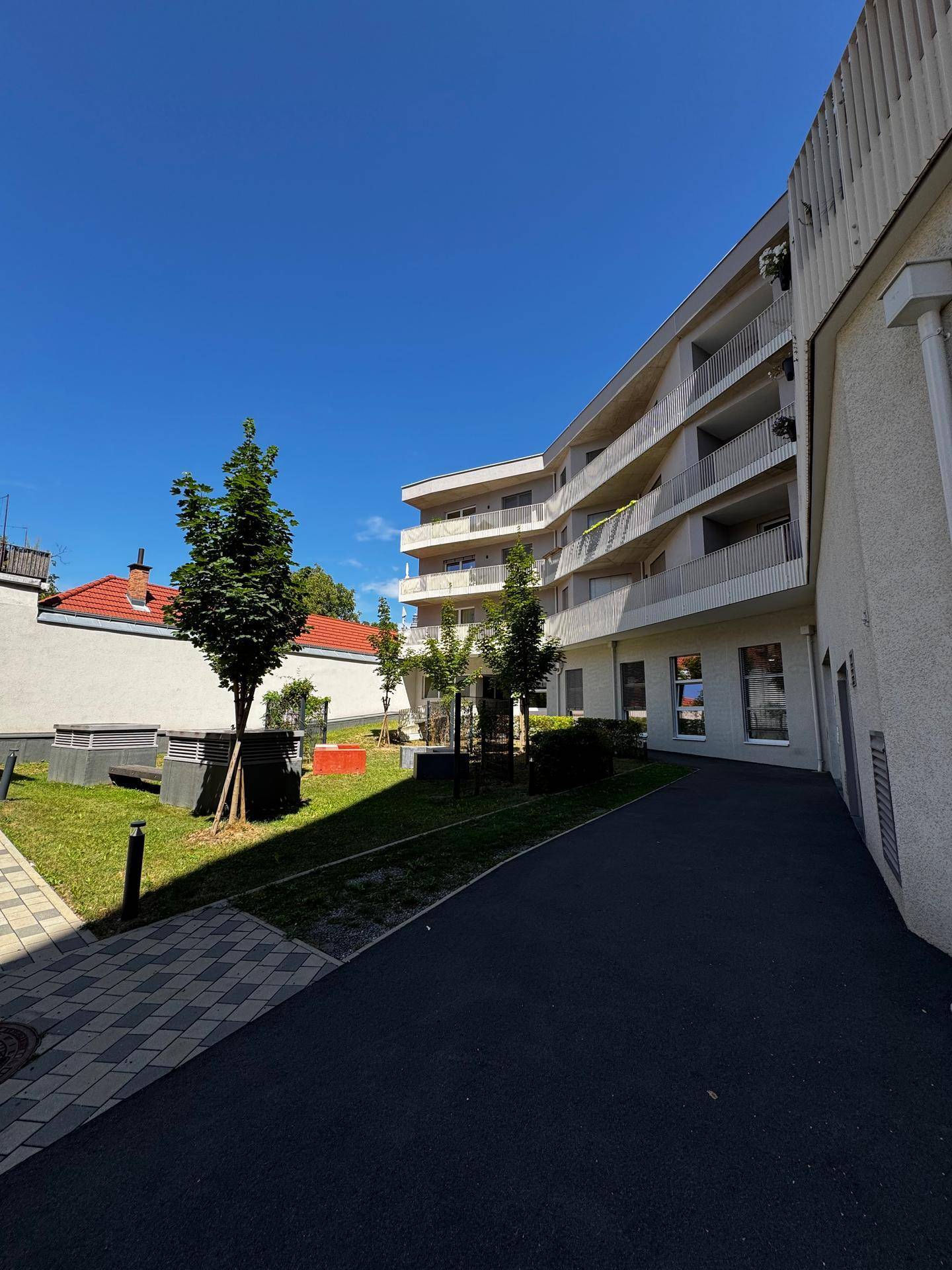 Gepflegter Außenbereich des Wohnkomplexes mit Grünflächen, jungen Bäumen und Gehwegen.