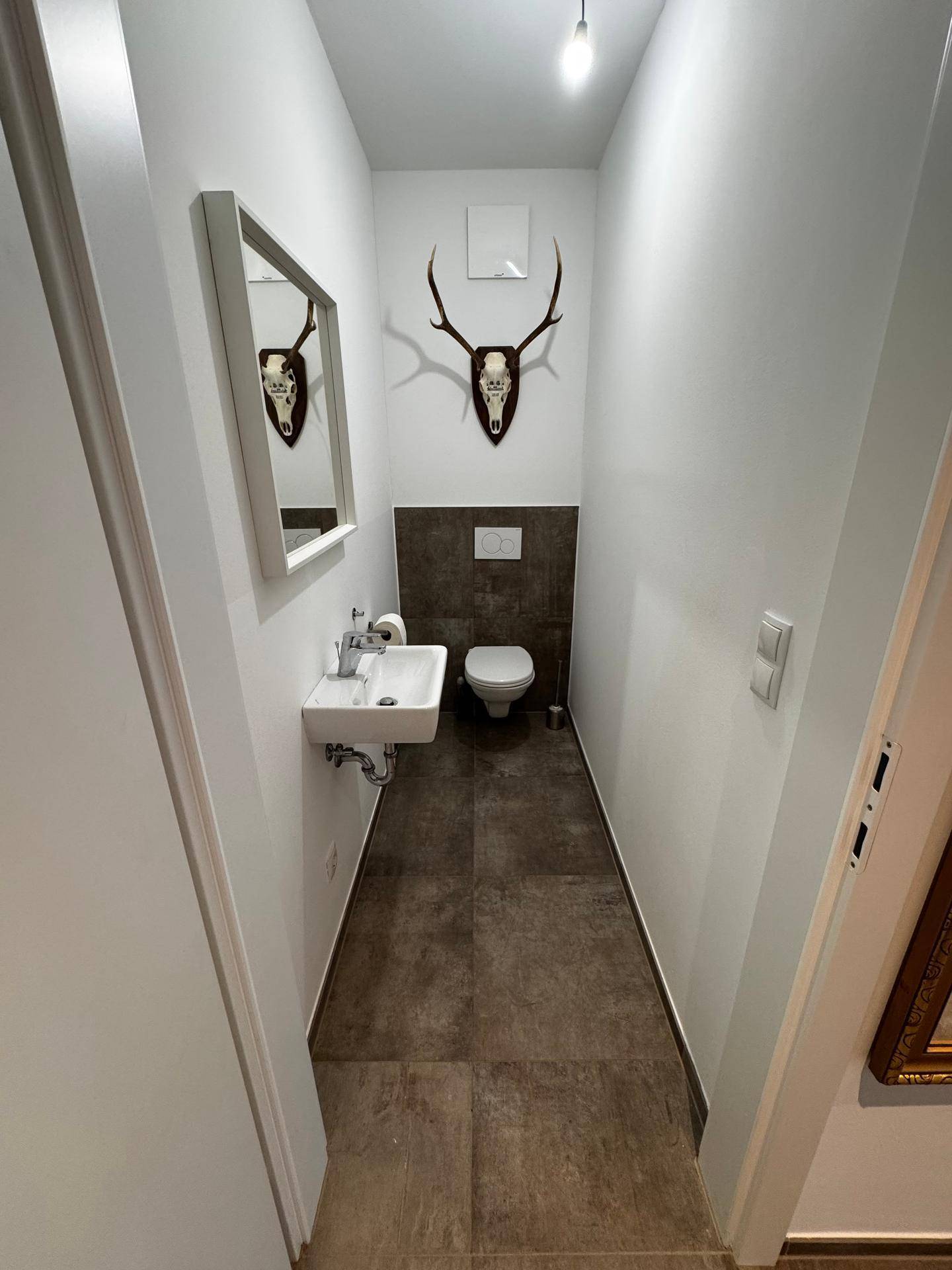 Modernes Gäste-WC mit Wand-WC, kleinem Waschbecken und dunklen Fliesen an Wand und Boden.