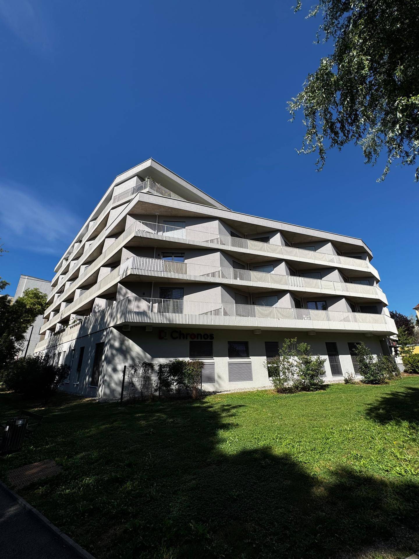 Modernes Mehrfamilienhaus mit vielen Balkonen und einer gepflegten Grünanlage im Vordergrund.