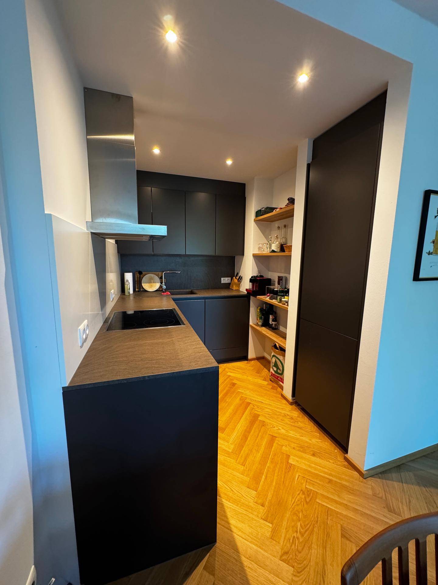Moderne Einbauküche mit schwarzen Fronten, Holzregalen und integrierten Edelstahlgeräten.