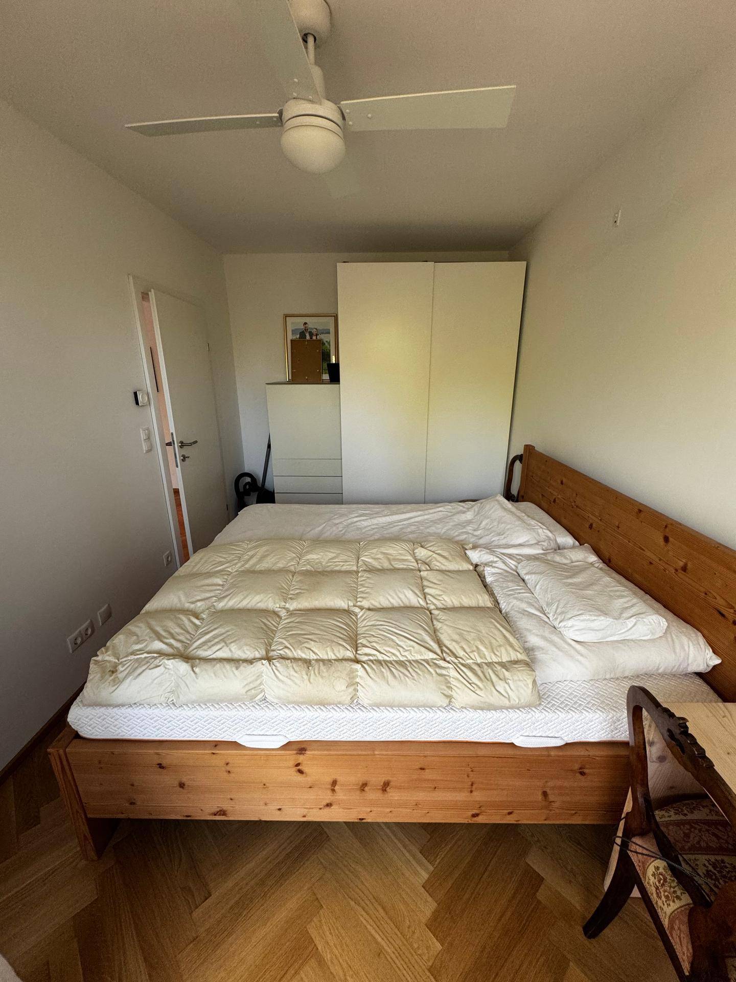 Schlafzimmer mit Holzbett, weißem Kleiderschrank und einem praktischen Deckenventilator.