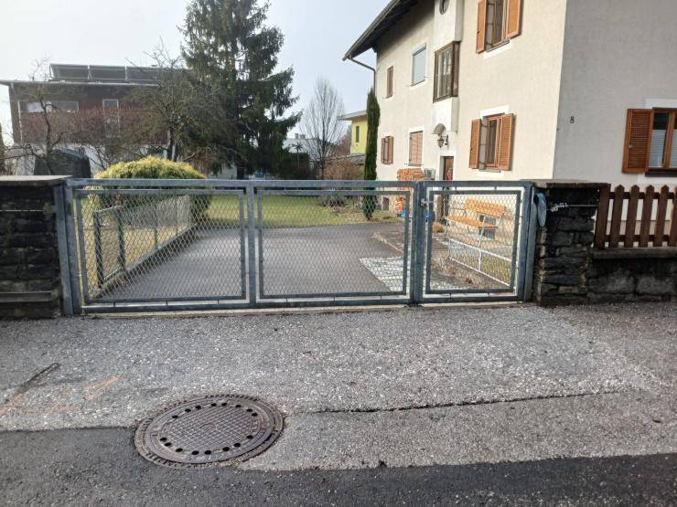 Einfahrt mit Metalltor und Kiesfläche vor einem Wohngebäude.