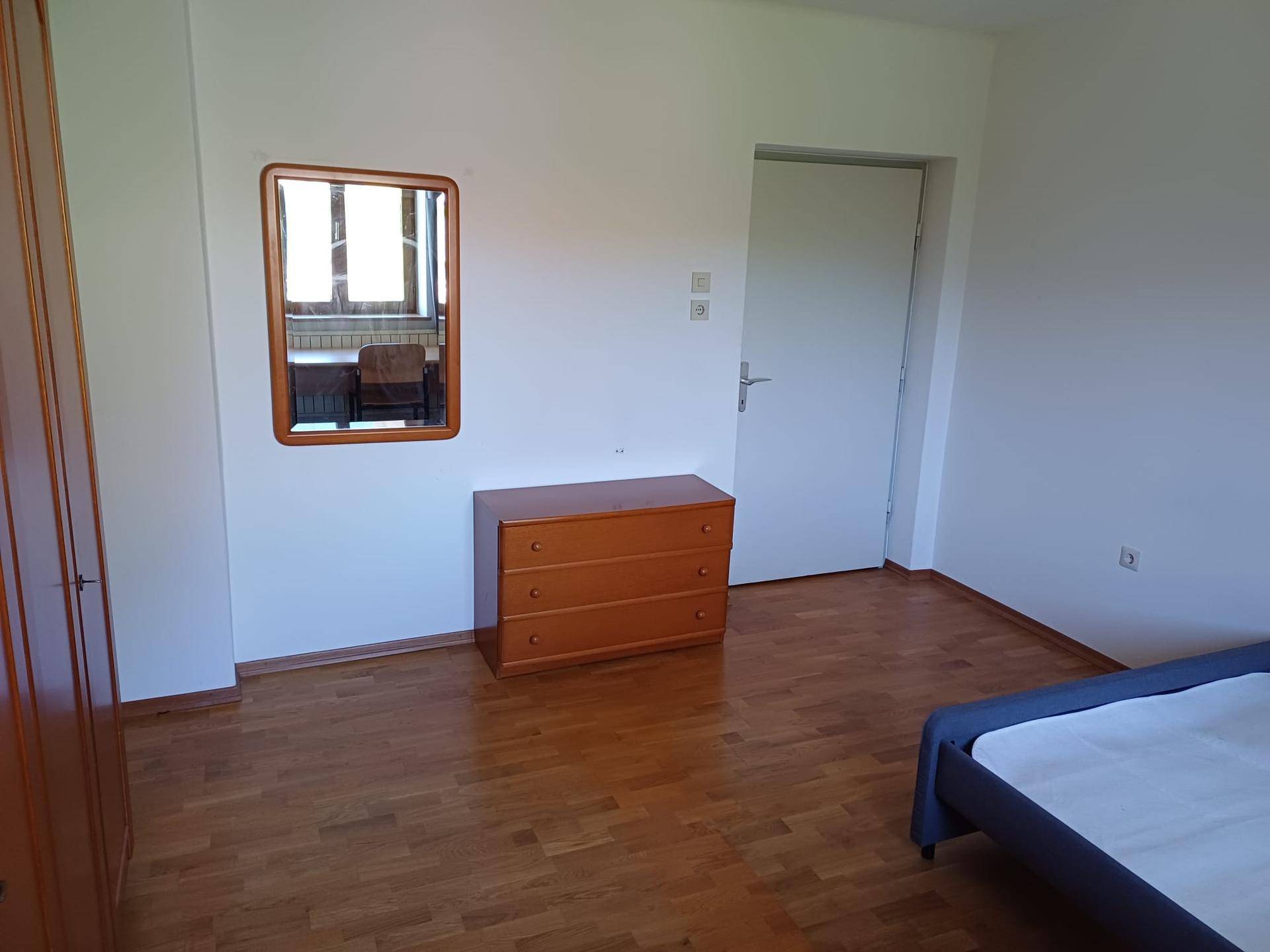 Schlafzimmer mit Holzboden, Kommode und Spiegel an der Wand.