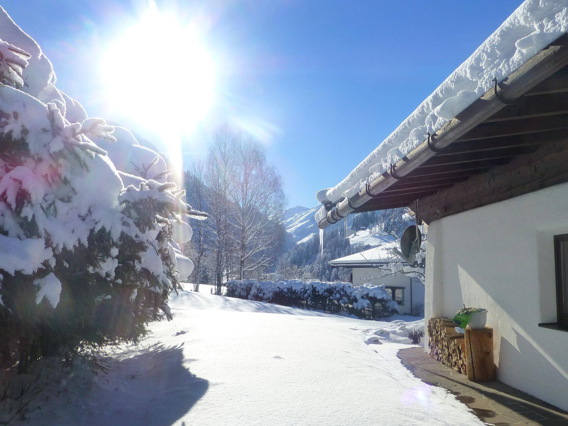 Sonnige Winteransicht des Hauses mit verschneitem Garten und strahlendem Himmel.