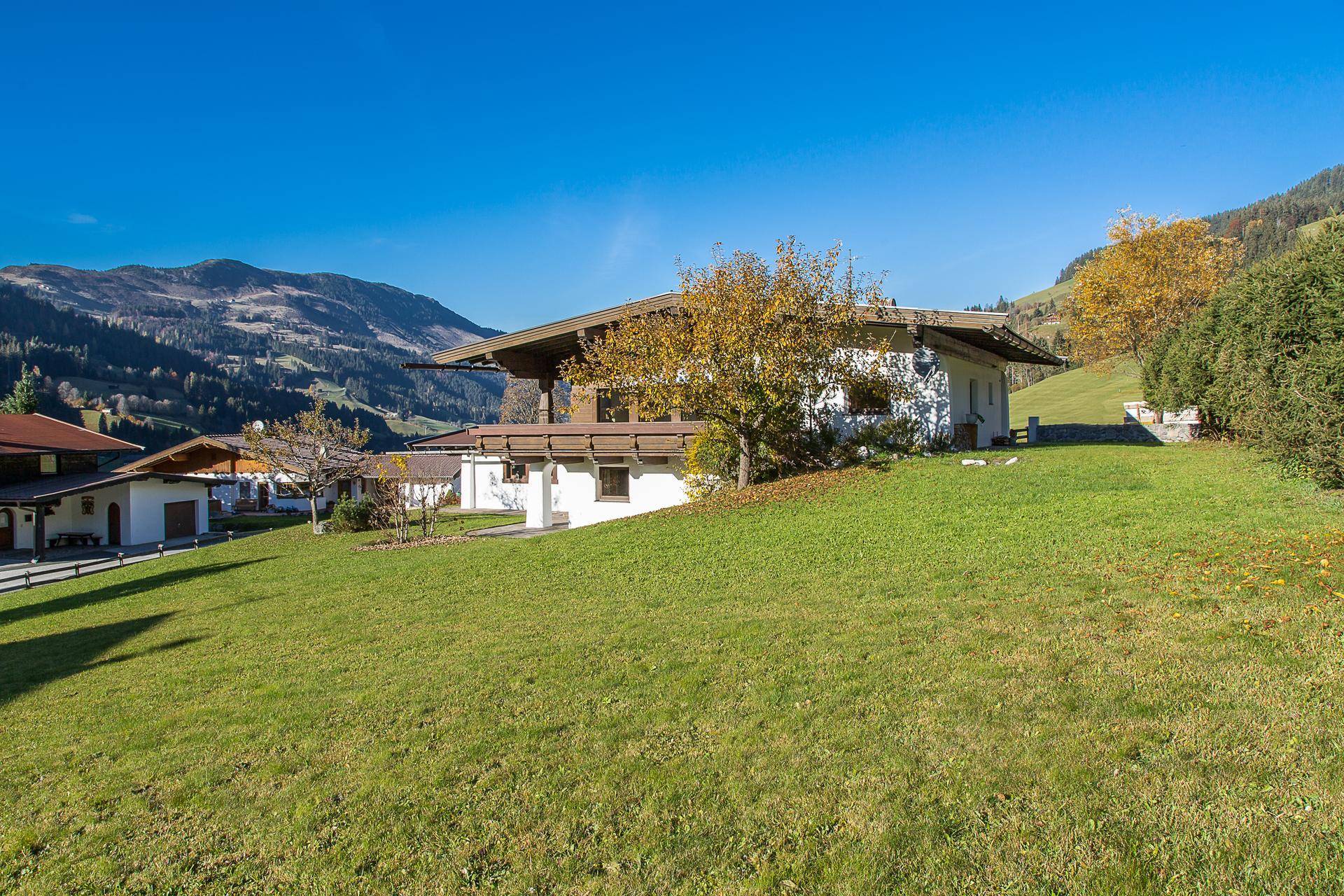 Haus im alpinen Stil mit breitem Dachüberstand und weißer Fassade auf einem grünen Hang mit Bergblick.