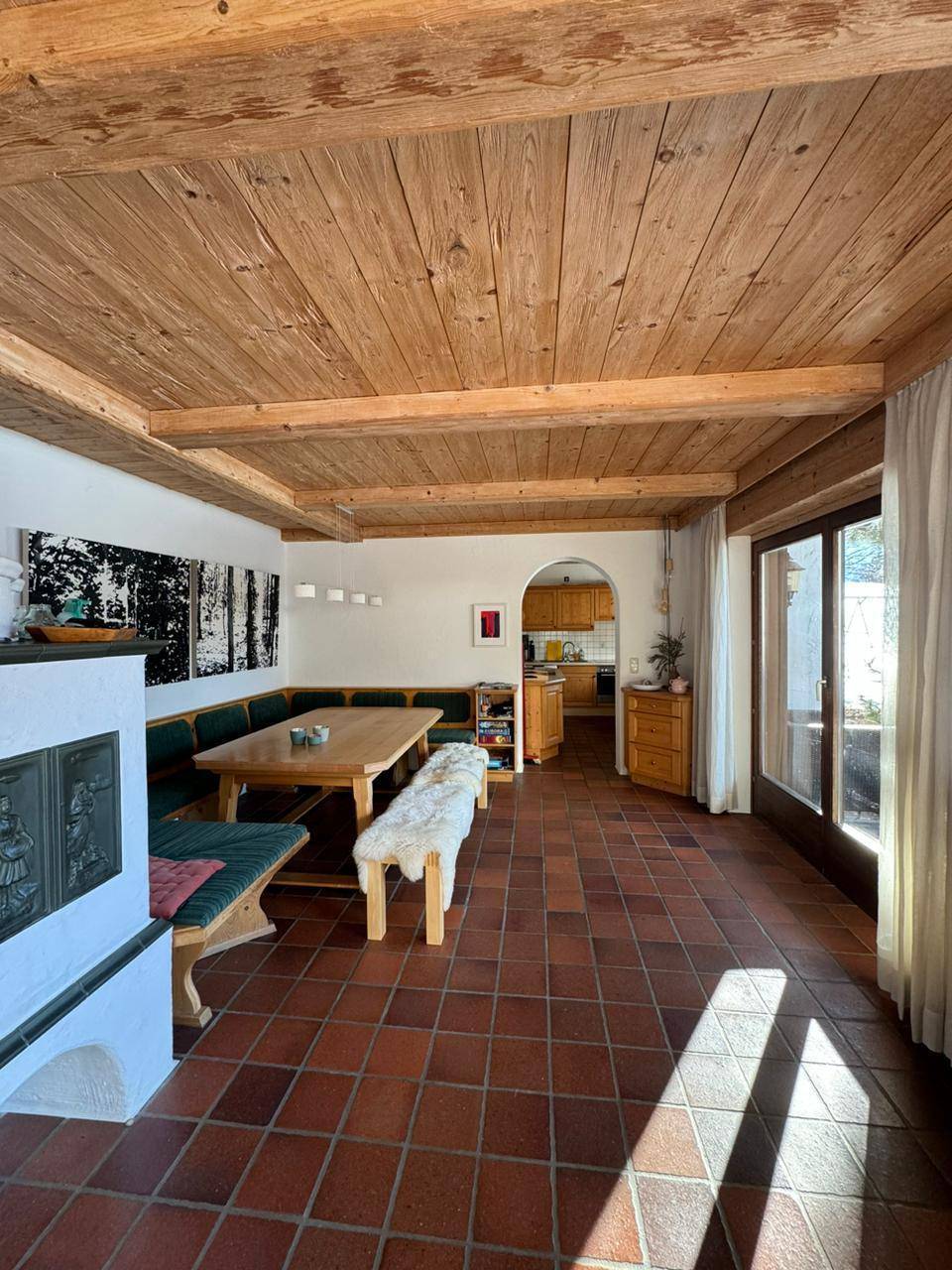 Gemütlicher Wohn-Essbereich mit Holzbalkendecke, Terrakottafliesen und traditionellem Kachelofen.