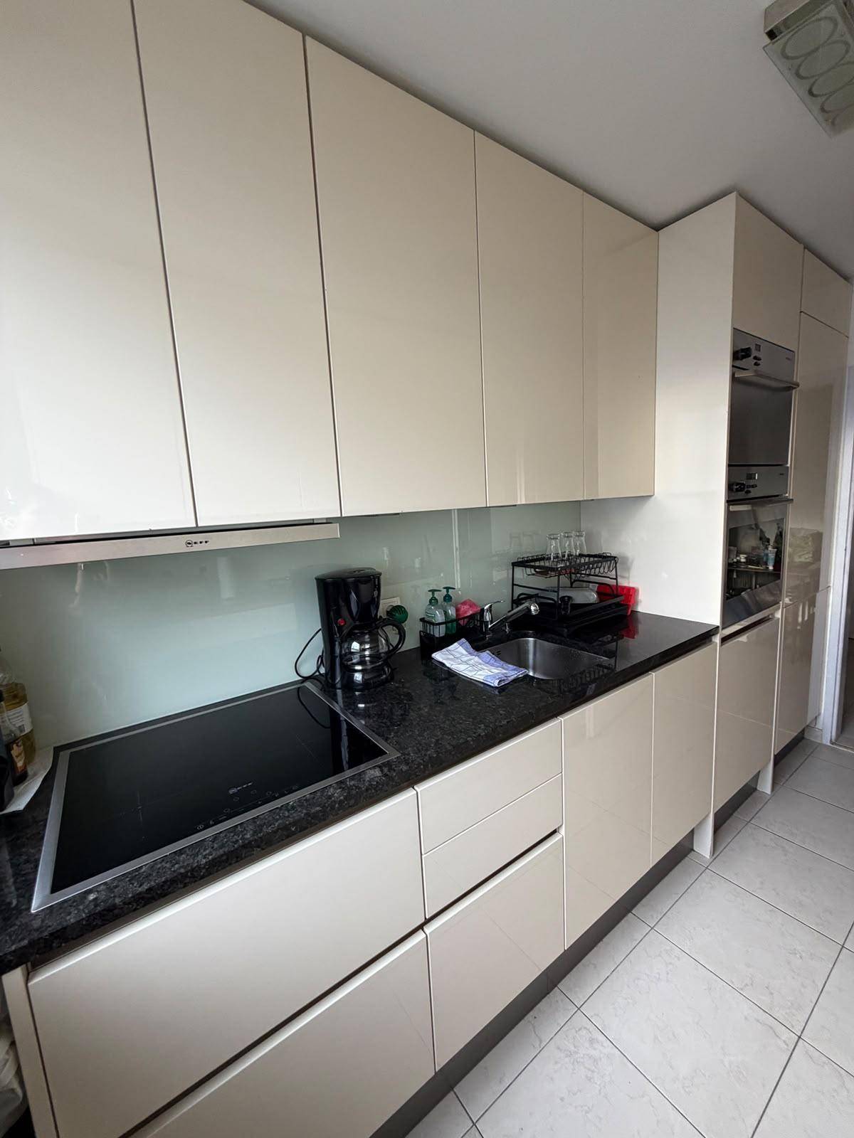 Moderne Küche mit beigen Hochglanzschränken, Induktionskochfeld und integrierten Geräten.
