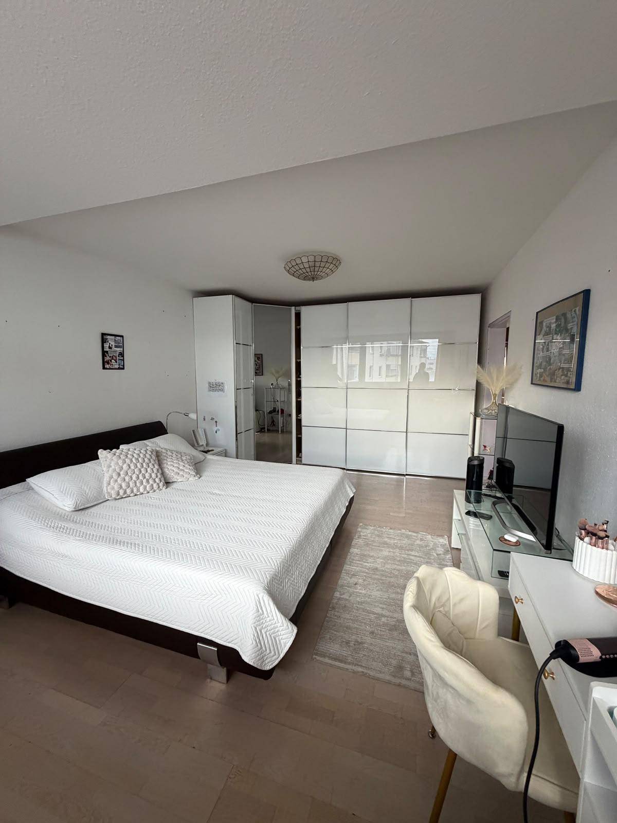 Schlafzimmer mit Doppelbett, hellem Laminatboden und weißen Schränken.