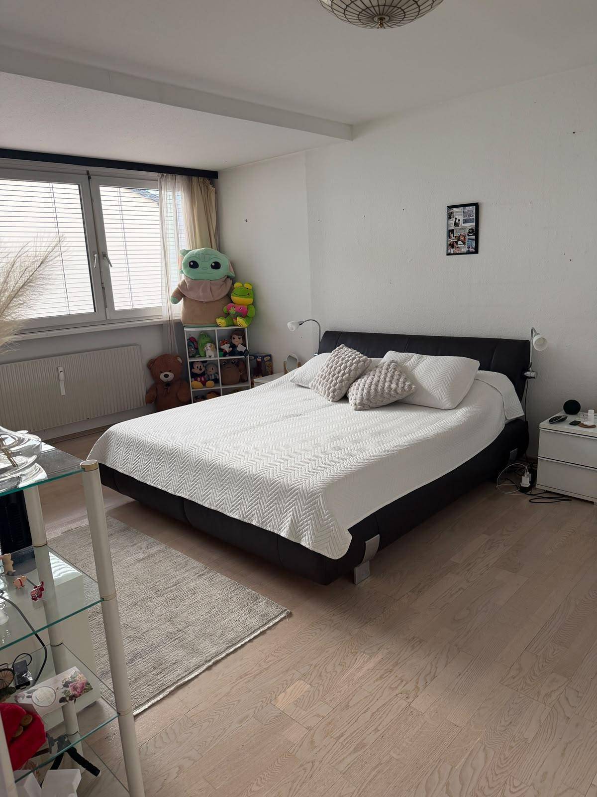 Schlafzimmer mit Doppelbett, hellem Laminatboden und Fenster mit Jalousien.