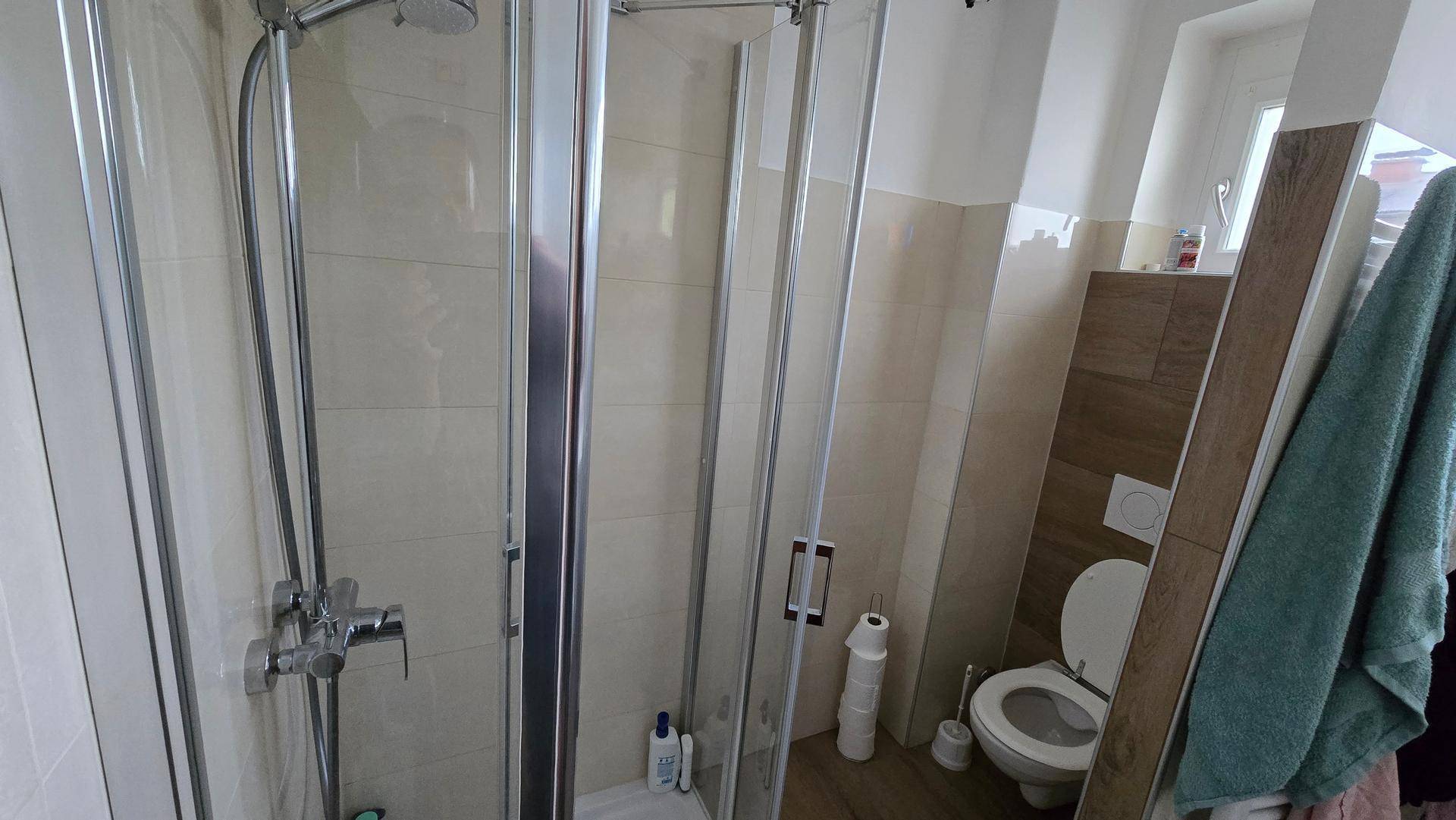 Badezimmer mit Duschkabine und Toilette, hell gefliest und praktisch gestaltet für den täglichen Gebrauch.