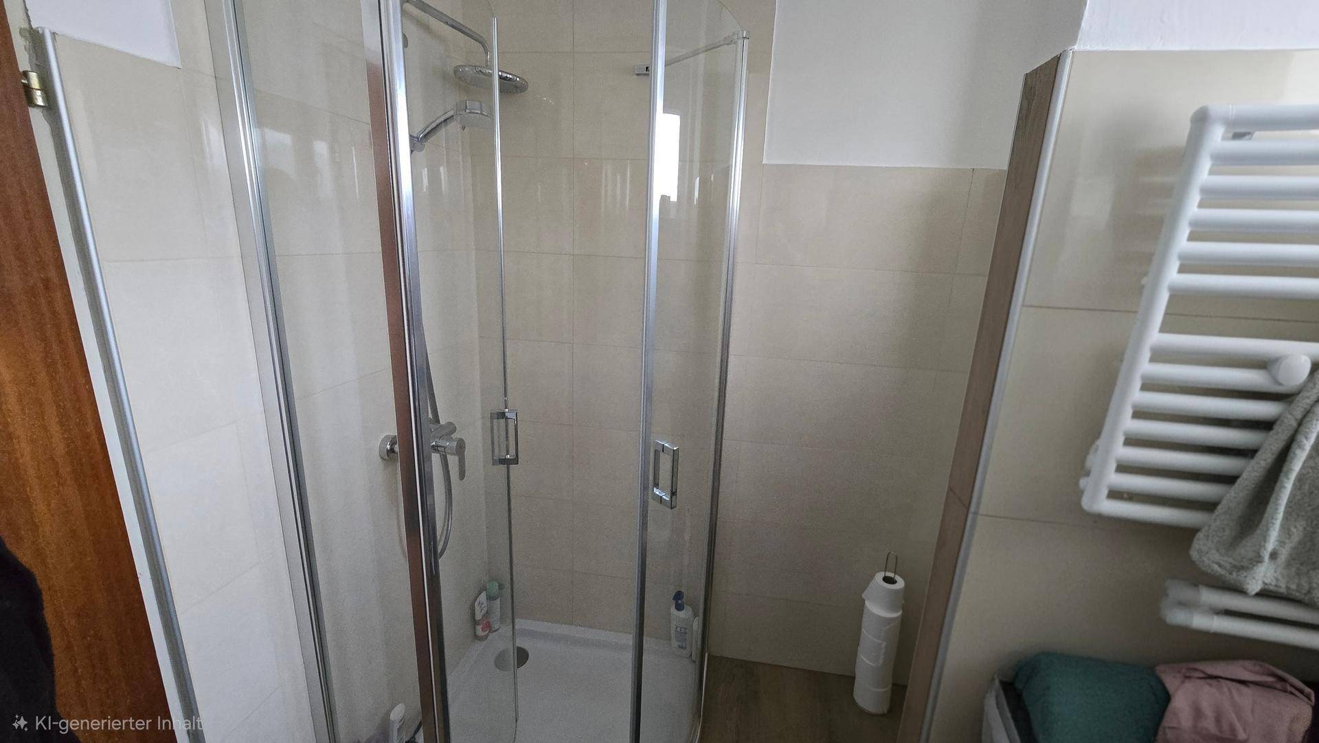 Duschbereich im Badezimmer mit Glasabtrennung und Handtuchheizkörper, sauber und modern gefliest.