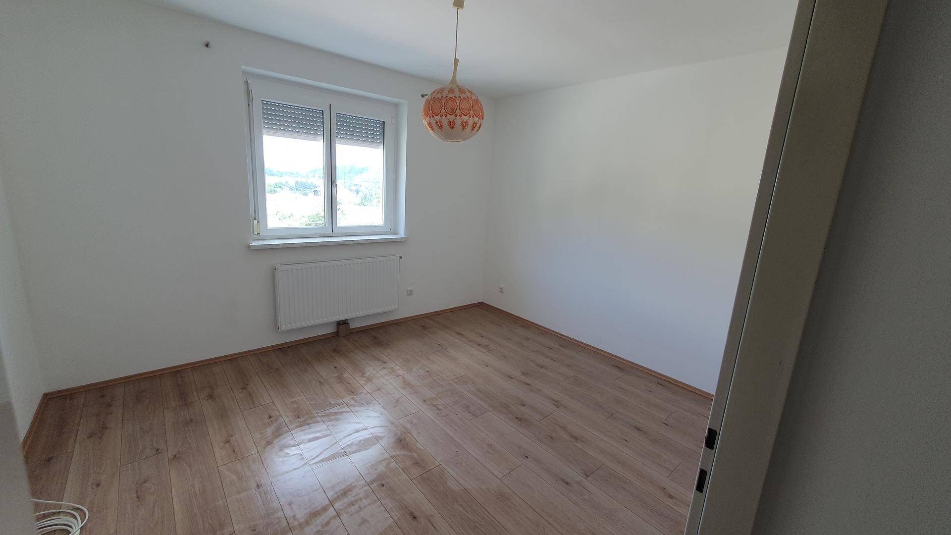 Helles Schlafzimmer mit Holzboden und Fenster, das einen angenehmen Ausblick und eine freundliche Atmosphäre schafft.