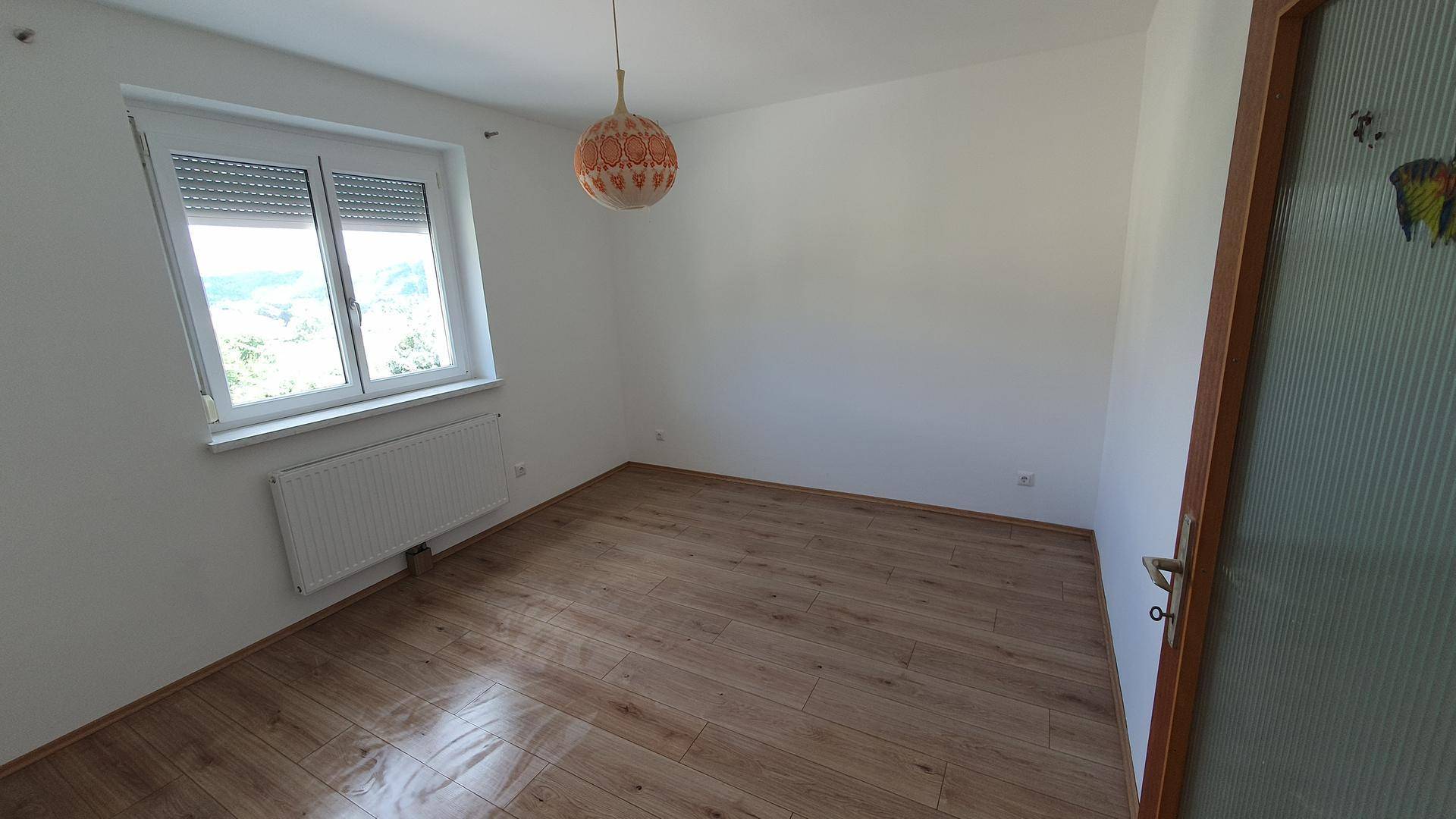 Geräumiges Schlafzimmer mit Holzboden und Fenster, das einen ruhigen Ausblick und viel Helligkeit bietet.