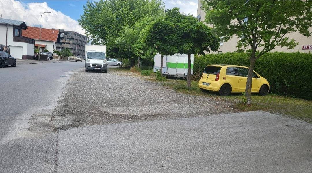 Außenansicht einer Wohngegend mit Parkplätzen, Bäumen, Hecken und einem geparkten gelben Auto.