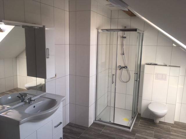Helles Badezimmer im Dachgeschoss mit Duschkabine, WC und Waschtisch unter Schrägdach.