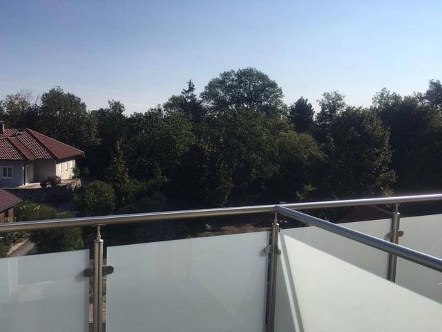 Blick vom Balkon mit Glasgeländer auf grüne Bäume und die umliegende Landschaft.