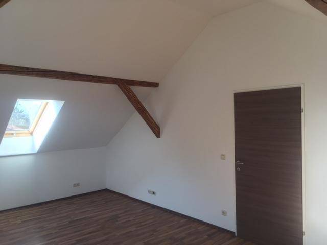 Geräumiger Dachgeschossraum mit Holzbalken, Dachfenster und dunkler Zimmertür.
