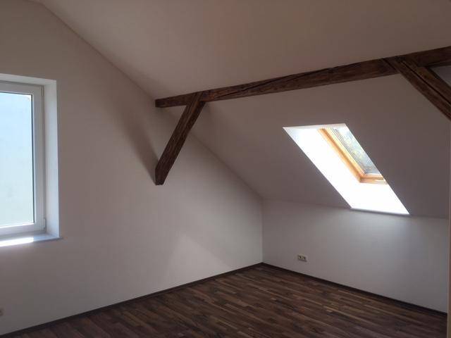 Lichtdurchfluteter Dachgeschossraum mit Fenster, Dachfenster und rustikalen Holzbalken.