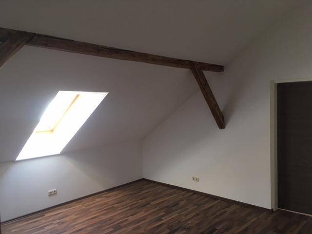 Geräumiger Dachgeschossraum mit Holzbalken, Dachfenster und Holzboden.