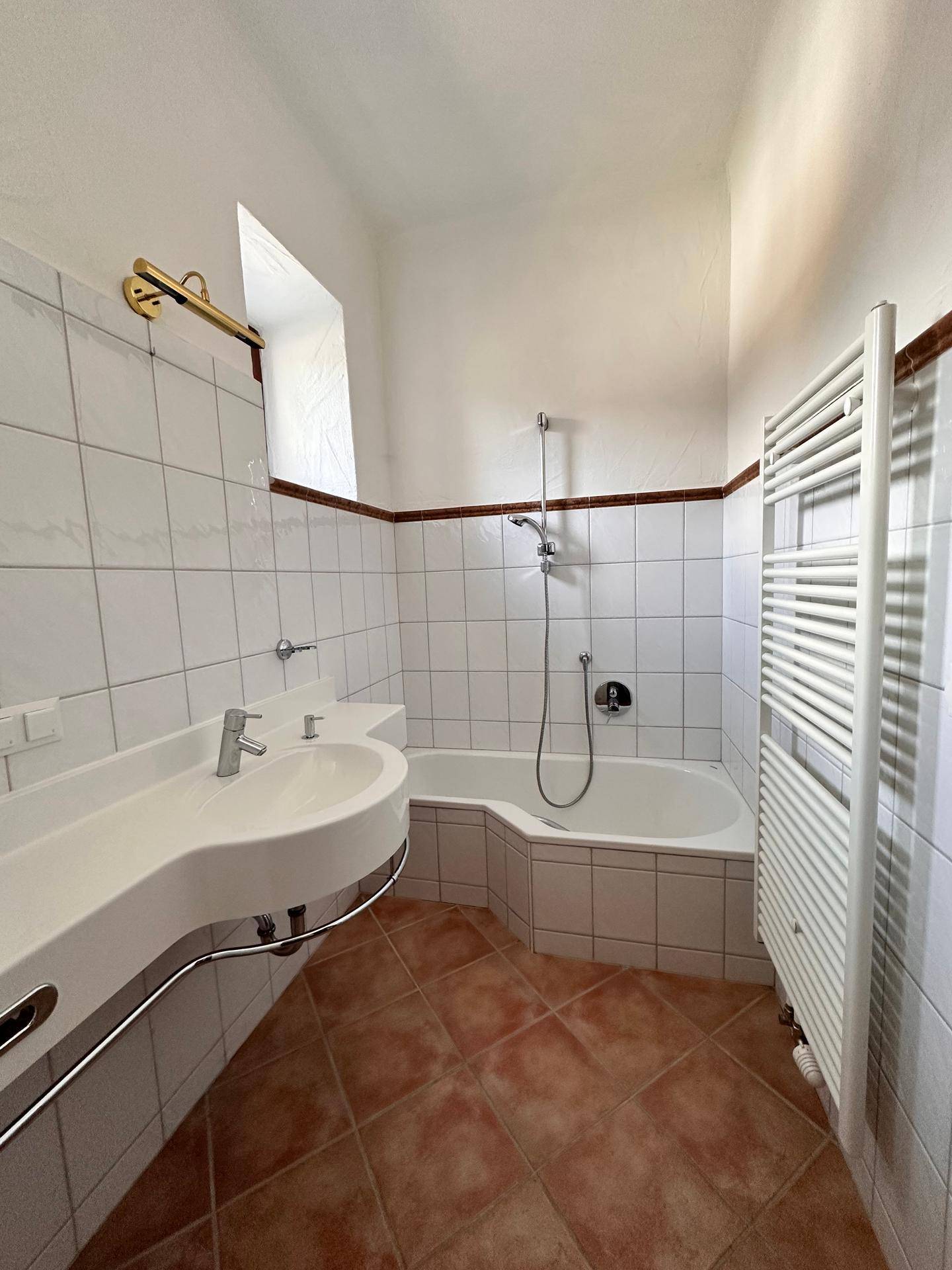 Badezimmer mit Badewanne, modernem Waschbecken und Terrakotta-Bodenfliesen.