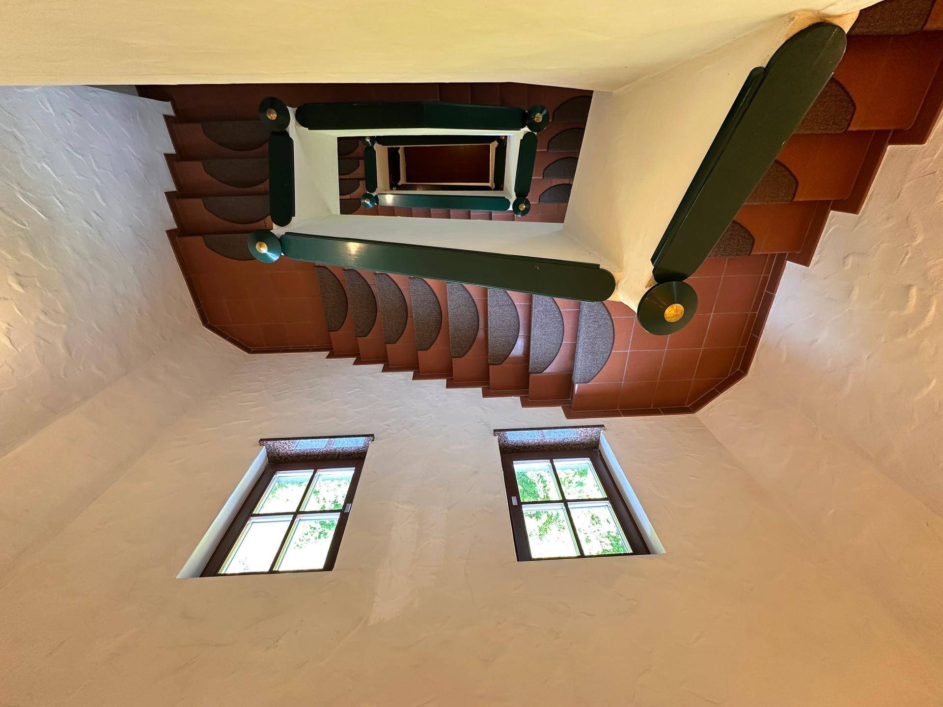 Wendeltreppe mit Terrakotta-Fliesen und Holzgeländer, von oben fotografiert.
