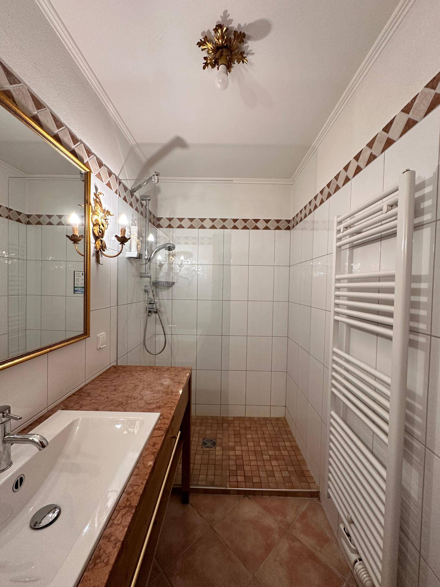 Badezimmer mit Duschbereich, weißen Fliesen und einem Waschtisch mit Marmorplatte.