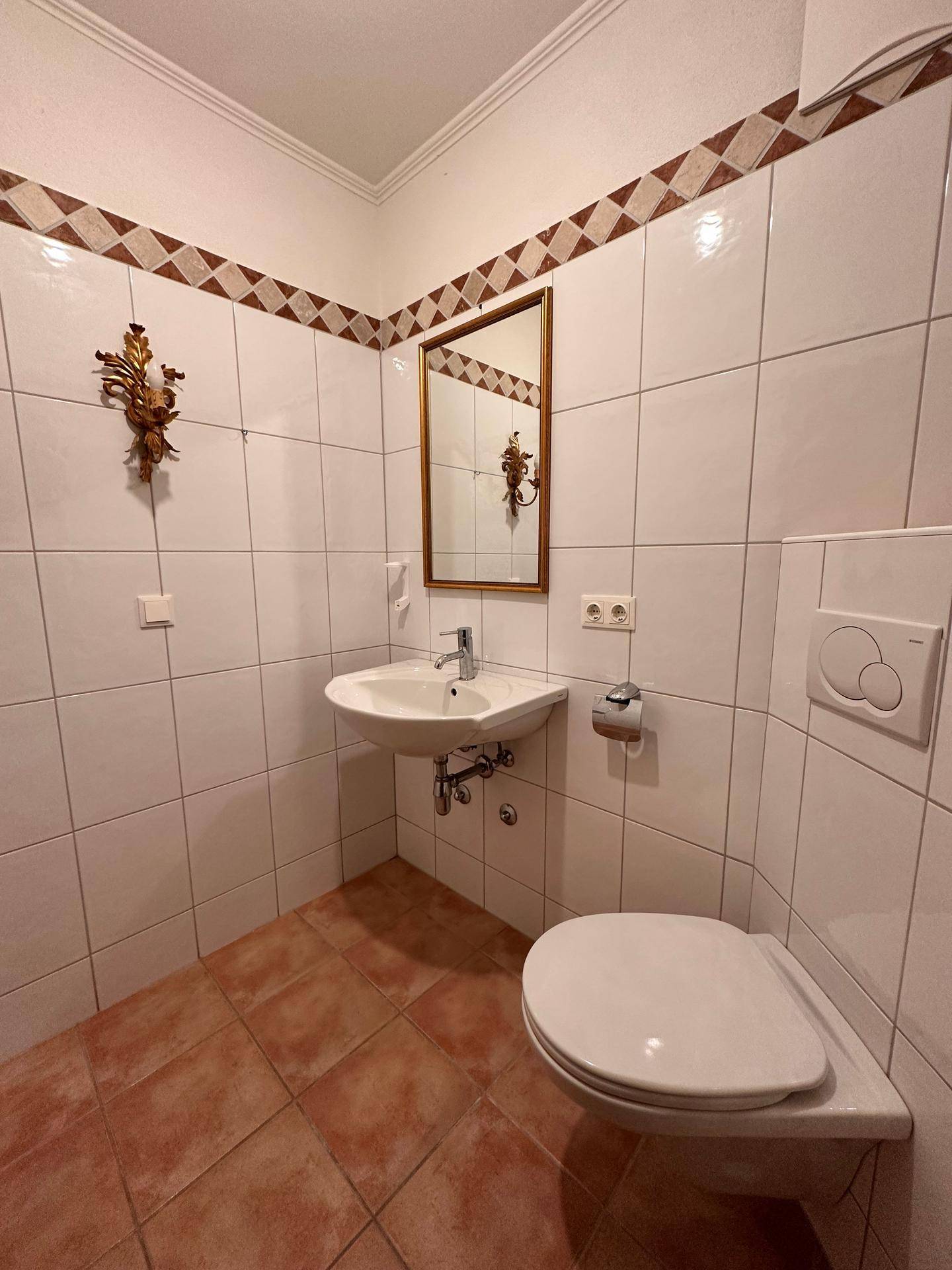 Gäste-WC mit weißen Wandfliesen, Terrakotta-Bodenfliesen und einem kleinen Waschbecken.