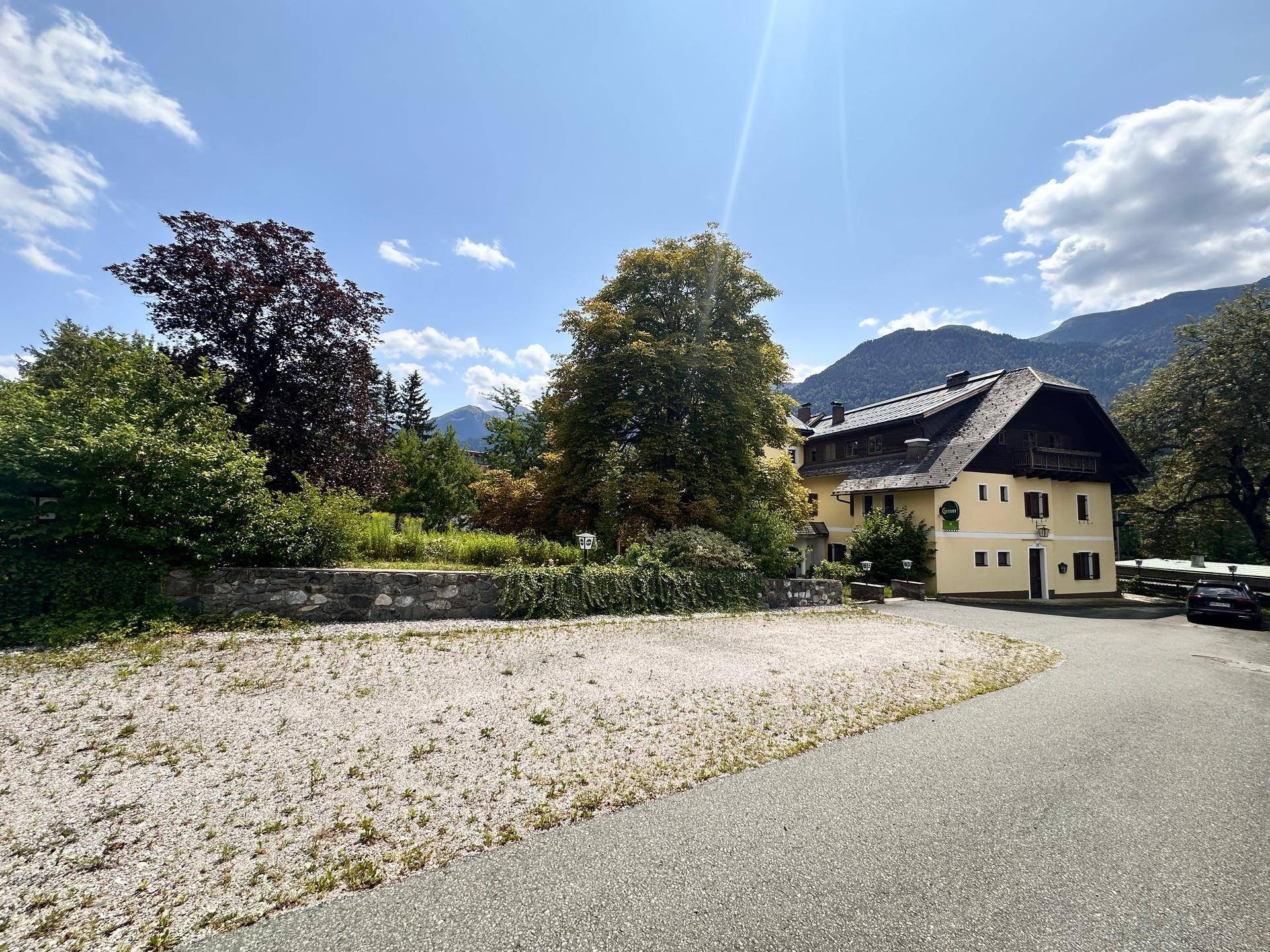 Großes Gebäude mit traditioneller Architektur, umgeben von Bäumen und Bergen unter blauem Himmel.