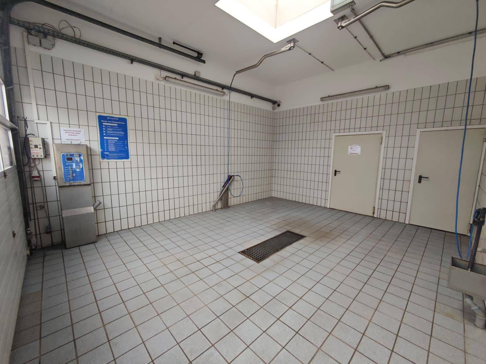 Innenansicht einer Waschbox mit gefliesten Wänden und Boden, ausgestattet für Fahrzeugreinigung.
