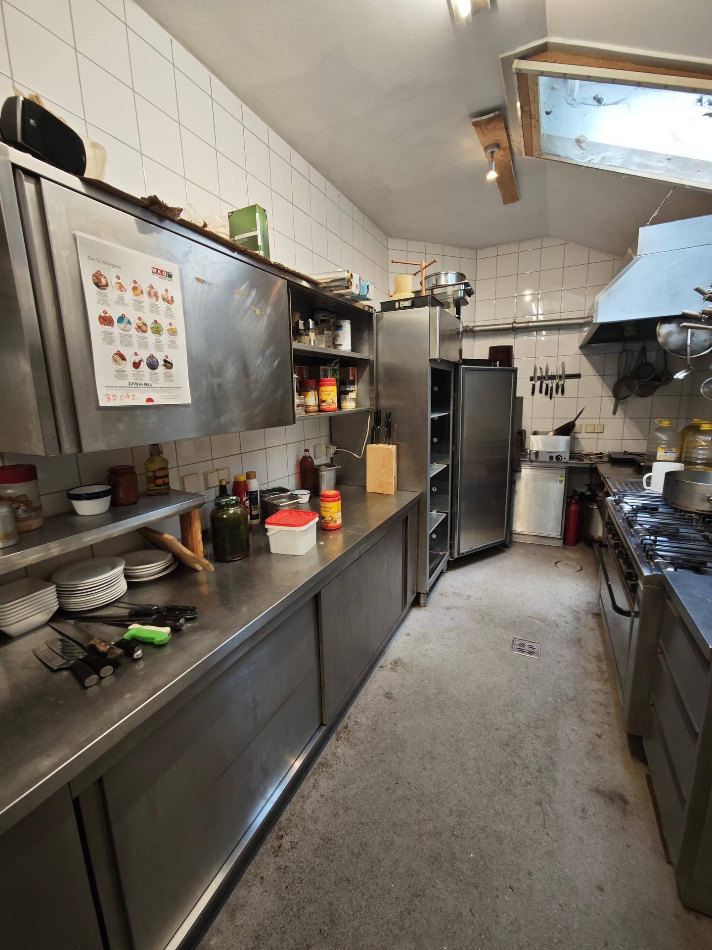 Professionelle Gastronomieküche mit Edelstahloberflächen, Fliesenwänden und industriellen Geräten.
