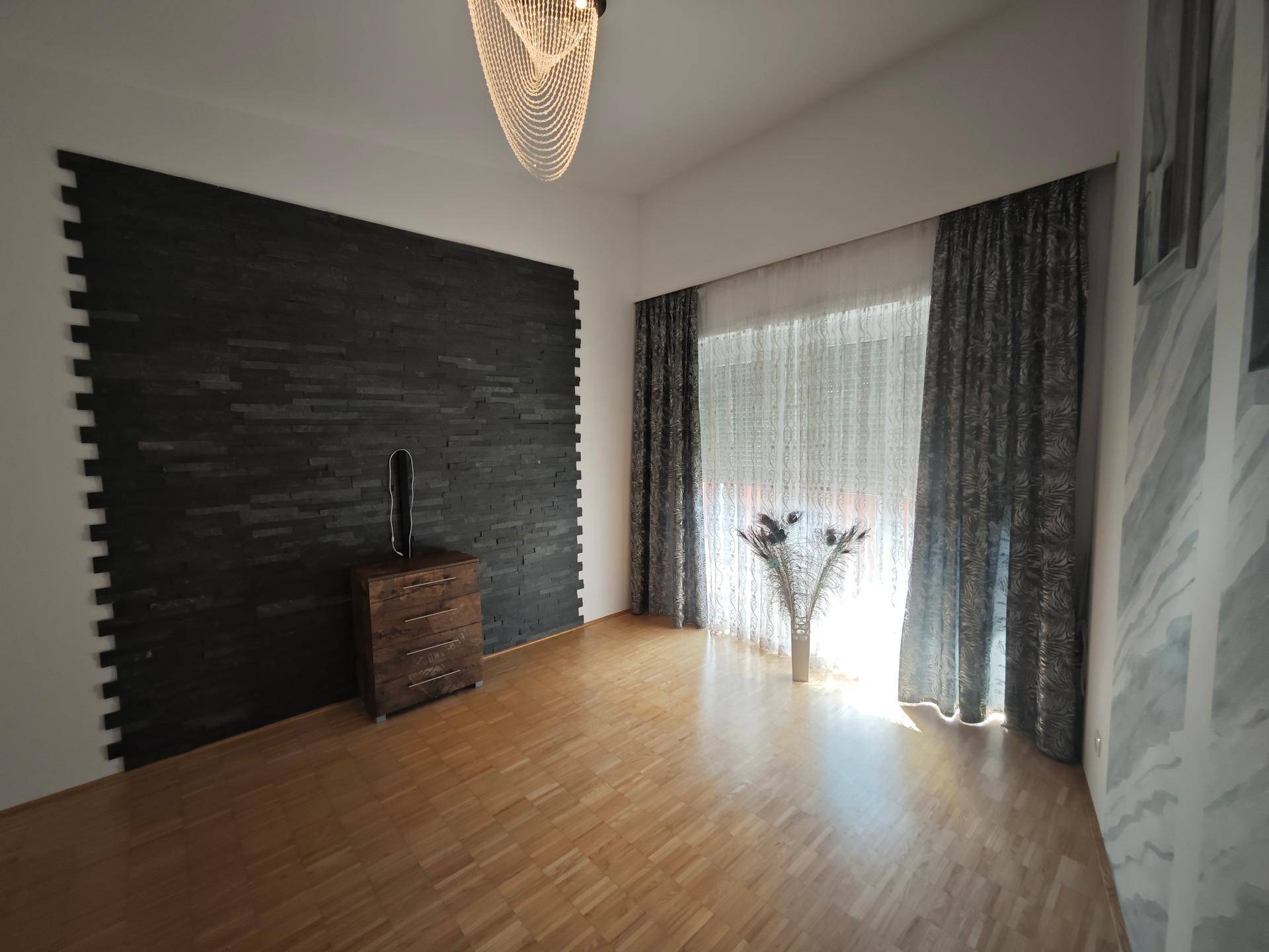 Geräumiger Raum mit Parkettboden, dunkler Akzentwand und großen Fenstern.