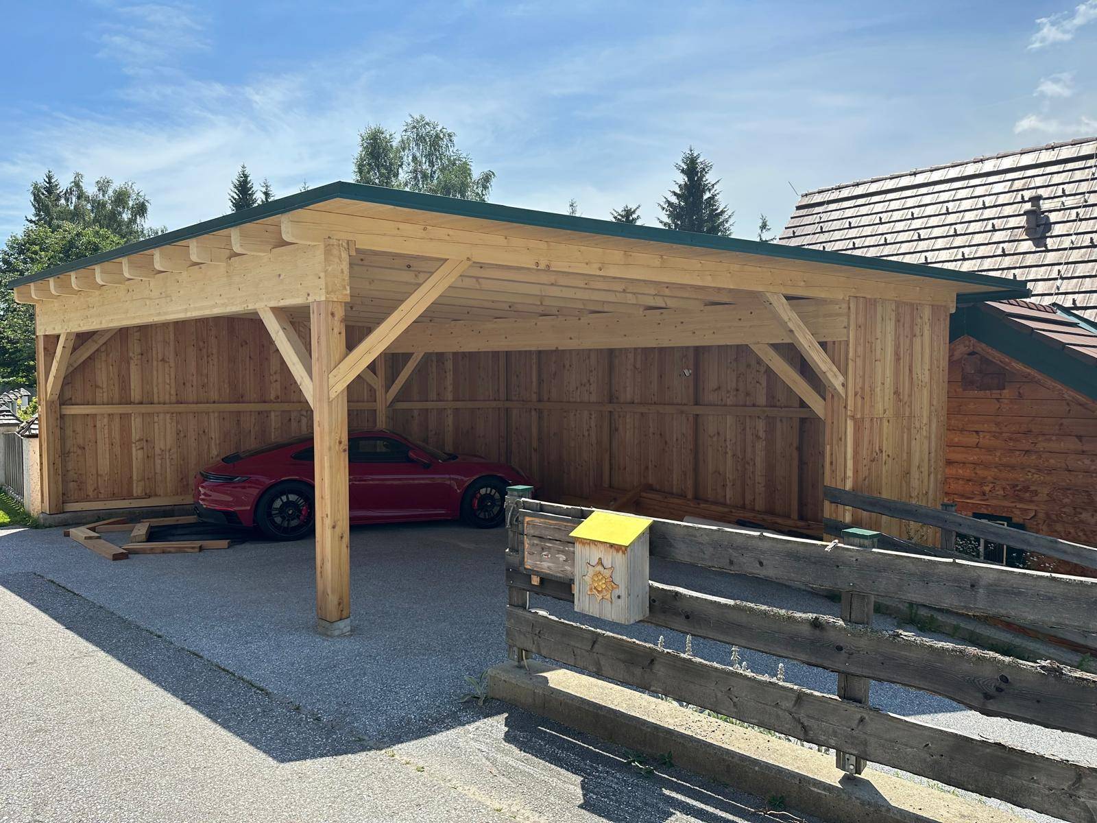 Offener Holzcarport mit Satteldach, bietet geschützten Parkplatz für ein Fahrzeug.